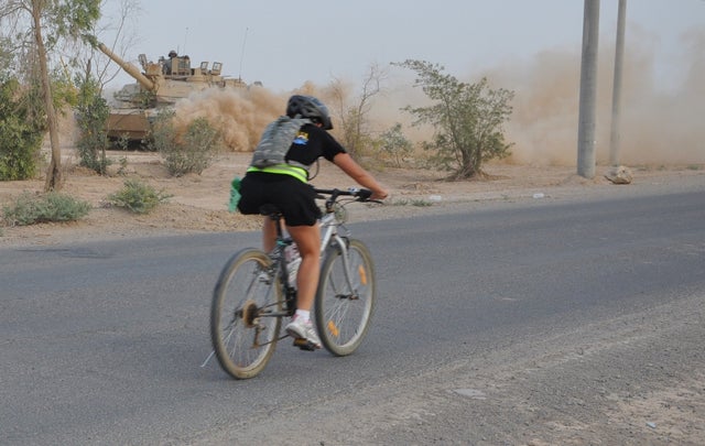 Staff Sgt. Patricia McCarthy, badging non-commissioned officer, Headquarters and Headquarters Co., 181st Brigade Support Battalion, and Olympia, Wash. native, rides past a M1A2 Abram tank during the Bushmaster’s Triathlon at Contingency Operation Base Q-West, Iraq, June 28. The race consisted of a 400-meter swim, an 11K bike and a 3K run.