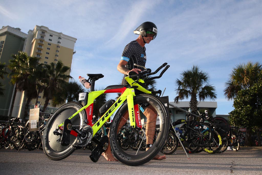 man walks triathlon bike outside during Ironman race