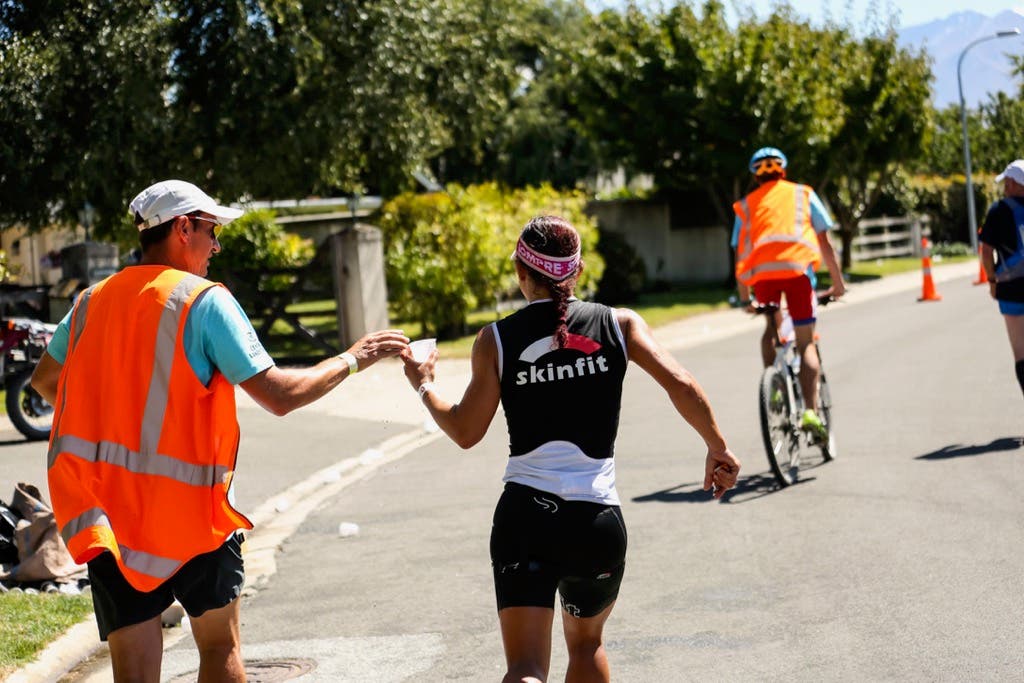 An athlete takes a drink to prevent quad cramps.