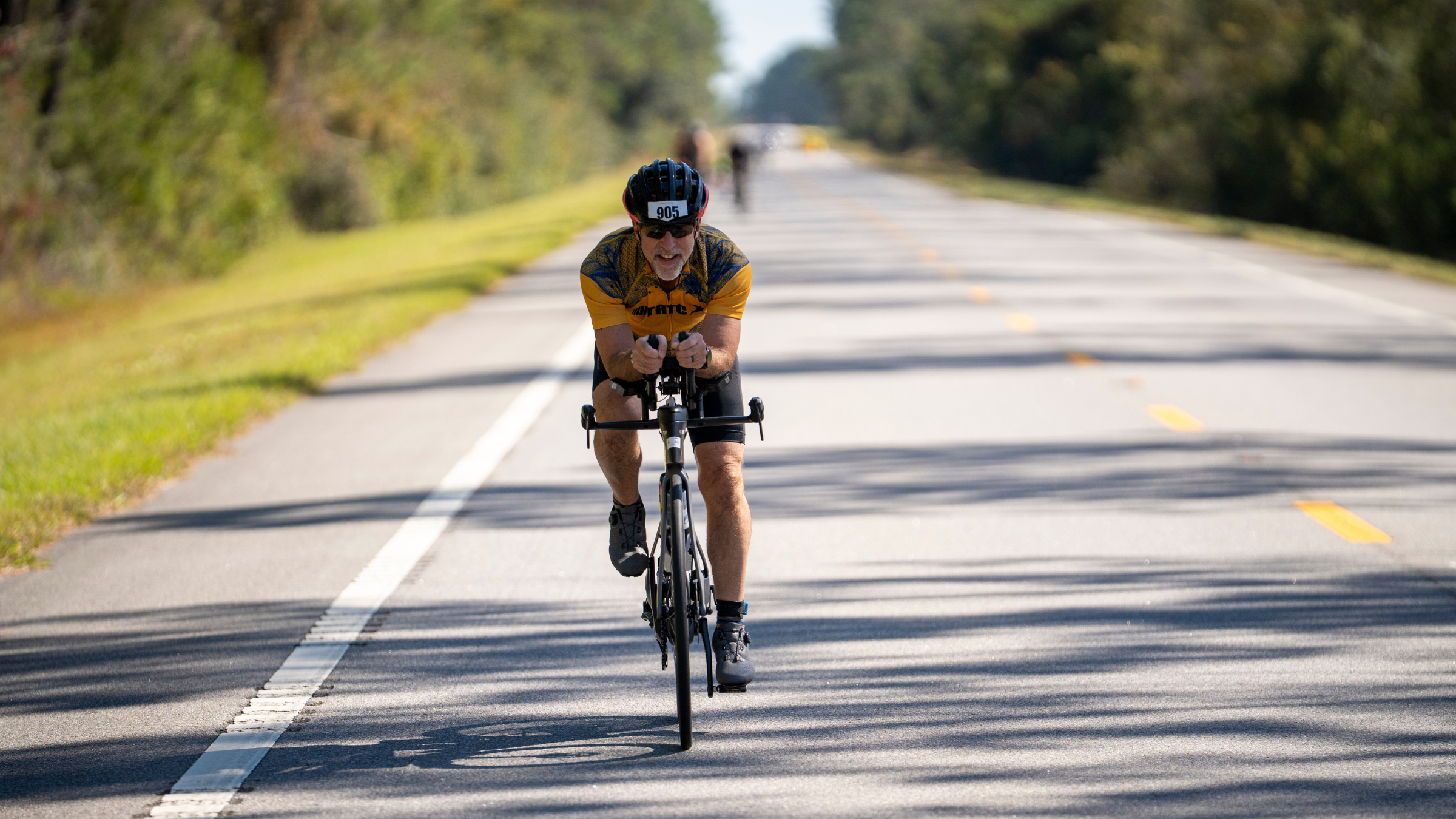 middle-aged man in yellow tri kit rides road bike toward camera on road in Ironman race