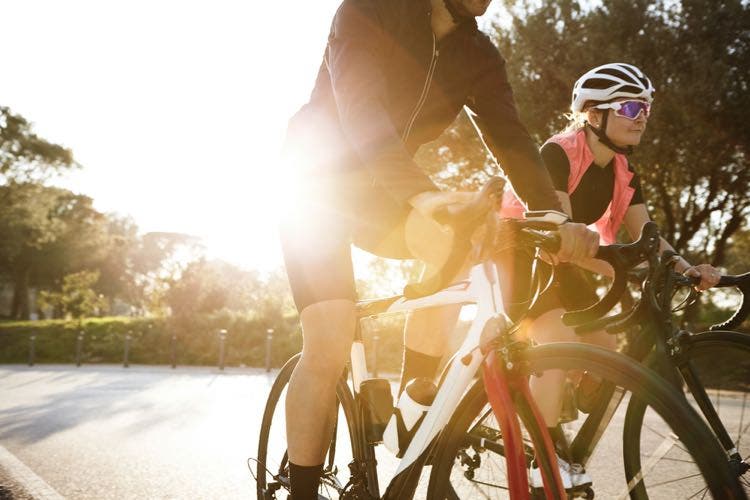 Two cyclists ride side-by-side while following cycling etiquette and using hand signals to stay safe.