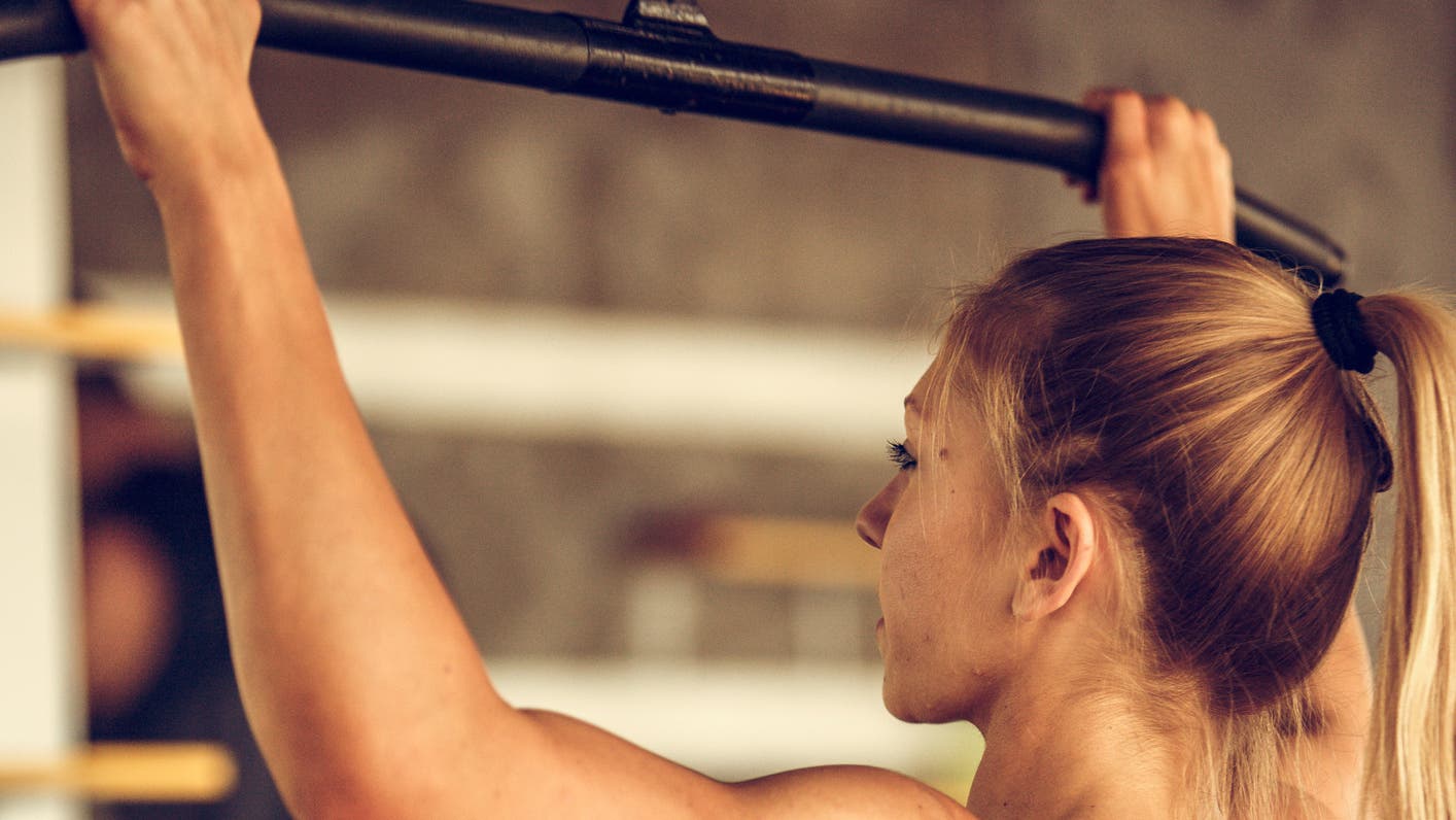 A women demonstrates a Straight-Arm Standing Lat Pulldown, an exercise that is great strength training for triathletes.