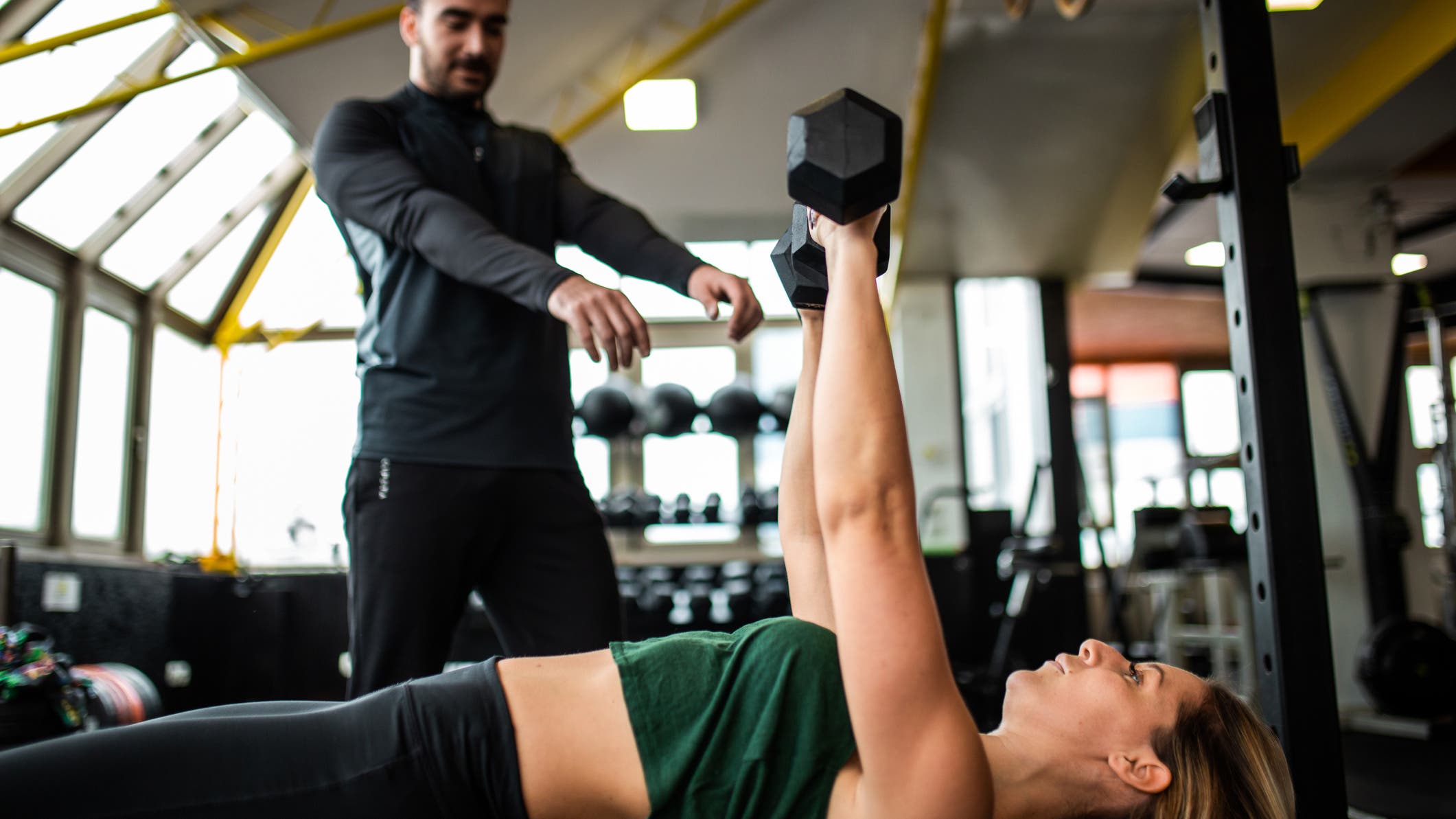 A women demonstrates an alternating dumbbell bench press, an exercise that is great strength training for triathletes.