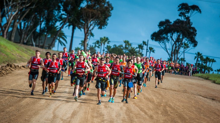 Crowd of swimrunners running toward camera on a tree-lined dirt road