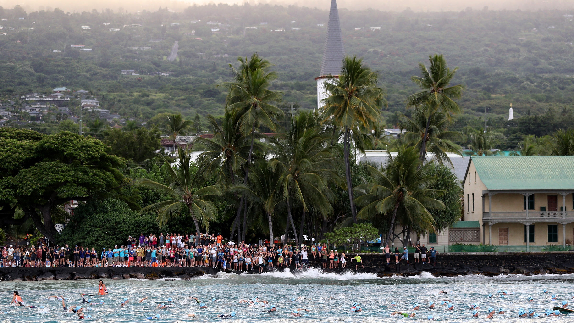 Athletes swim in the 2019 Ironman World Championship while a crowd looks on.