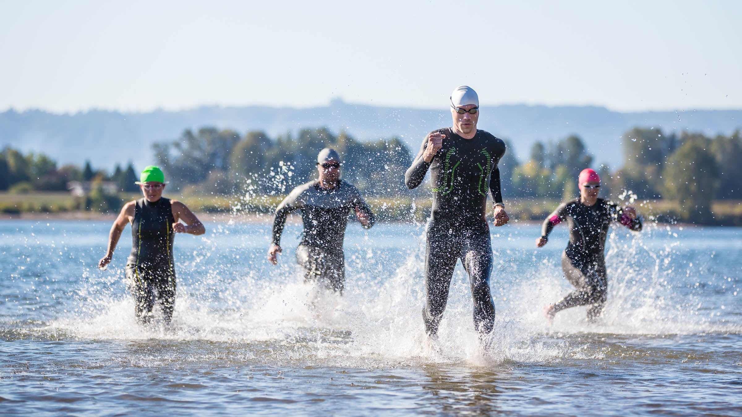 Four triathletes running out of the water