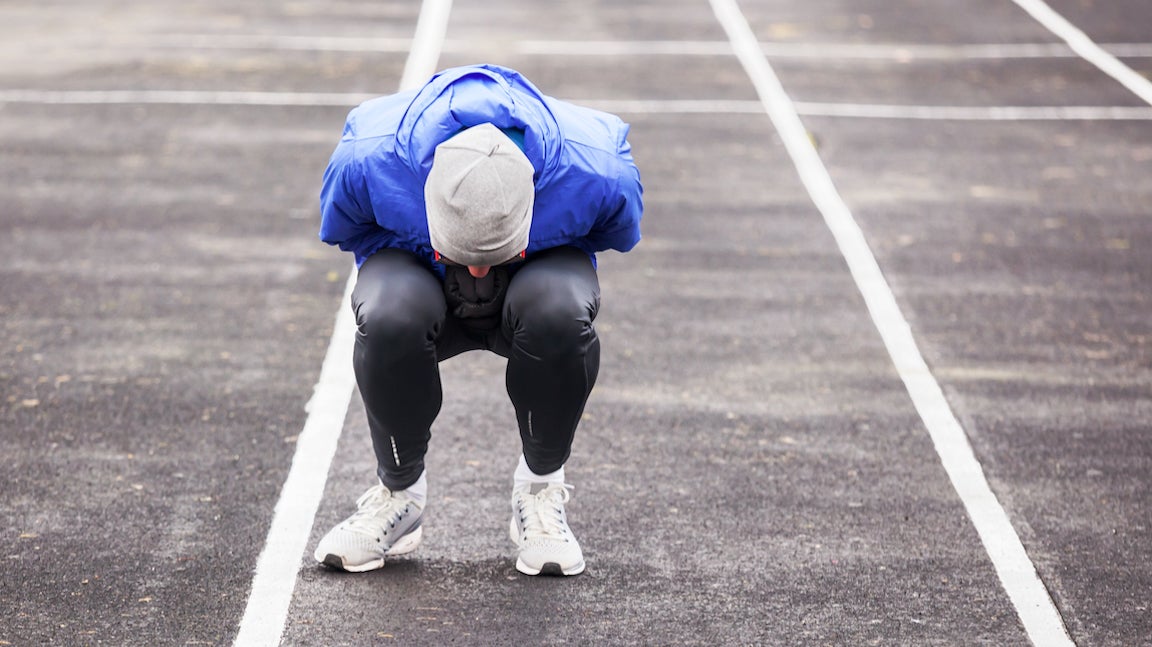 Male runner doubled over in pain on a track.
