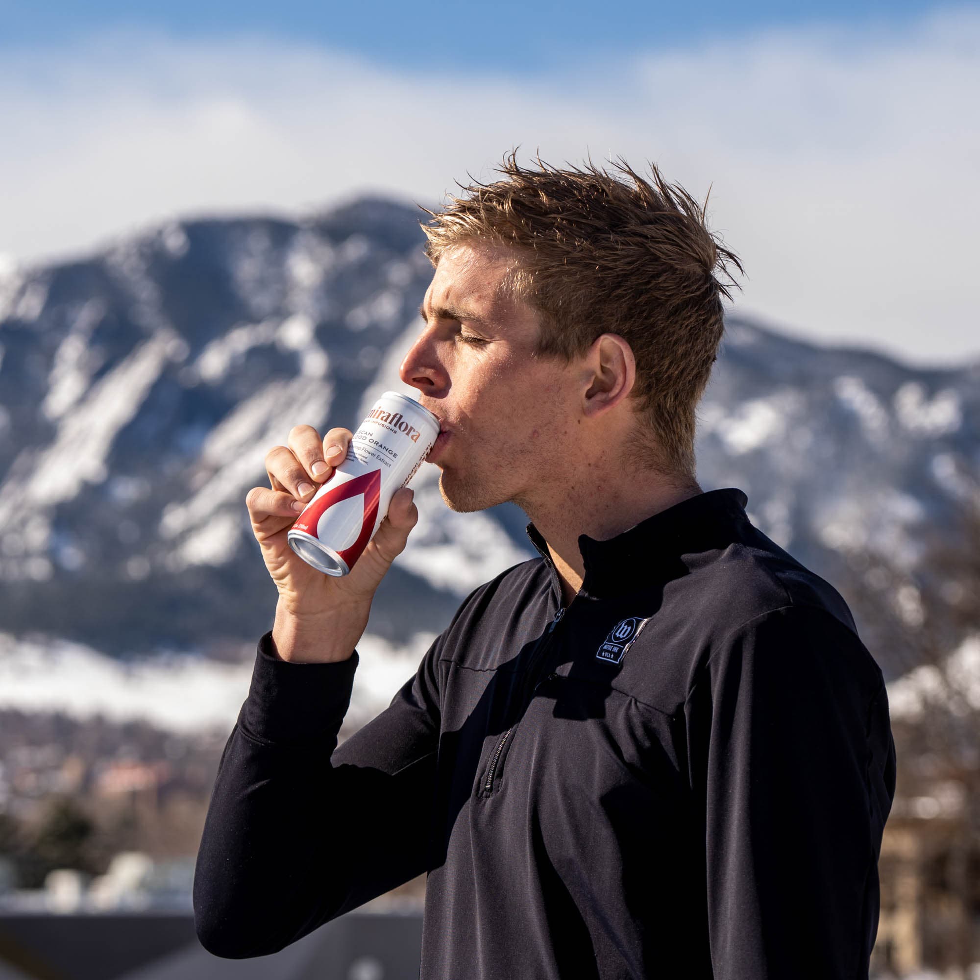 Sam Long drinking a Miraflora sparkling beverage in front of snow-covered mountains
