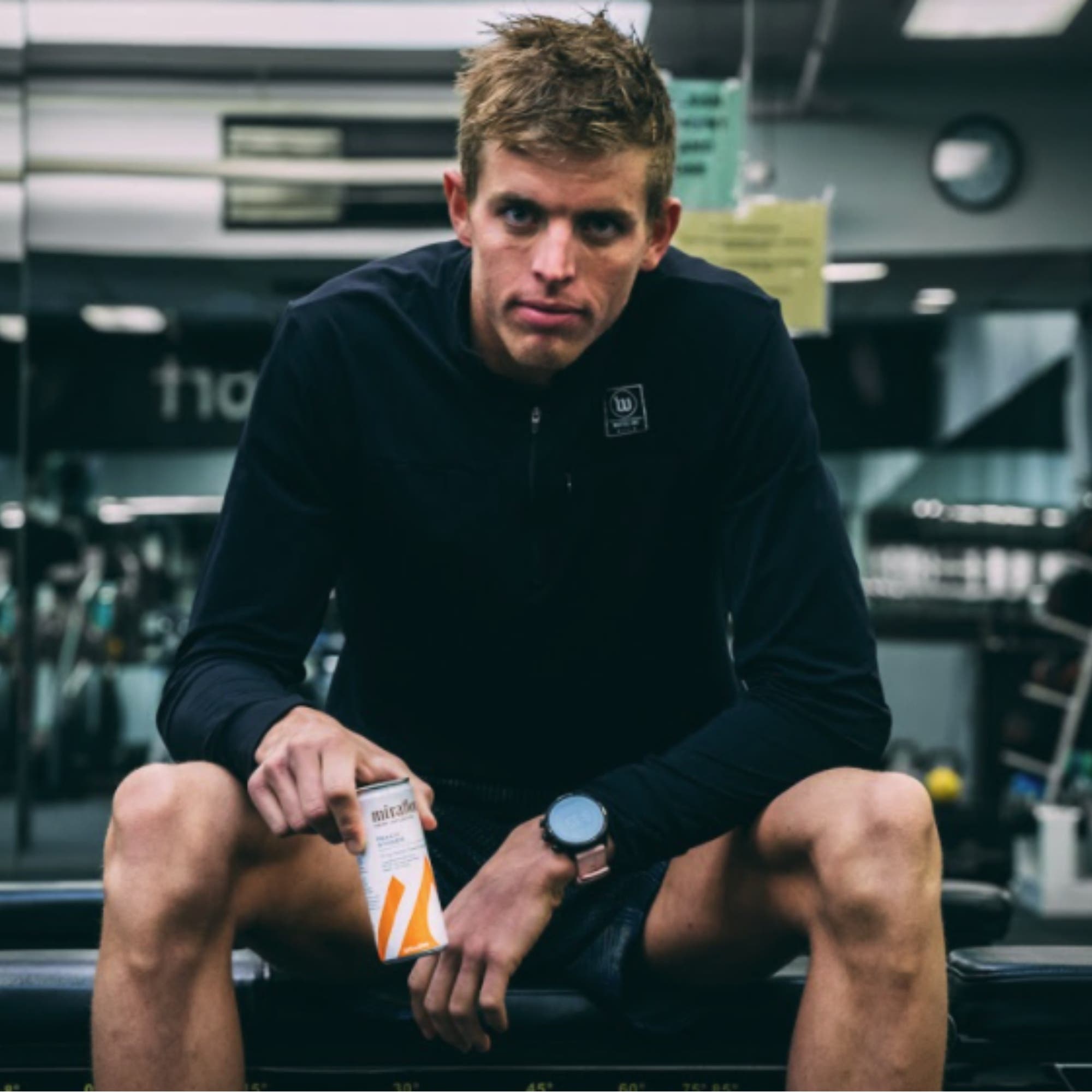 Sam Long sitting in the gym, holding a Miraflora drink can