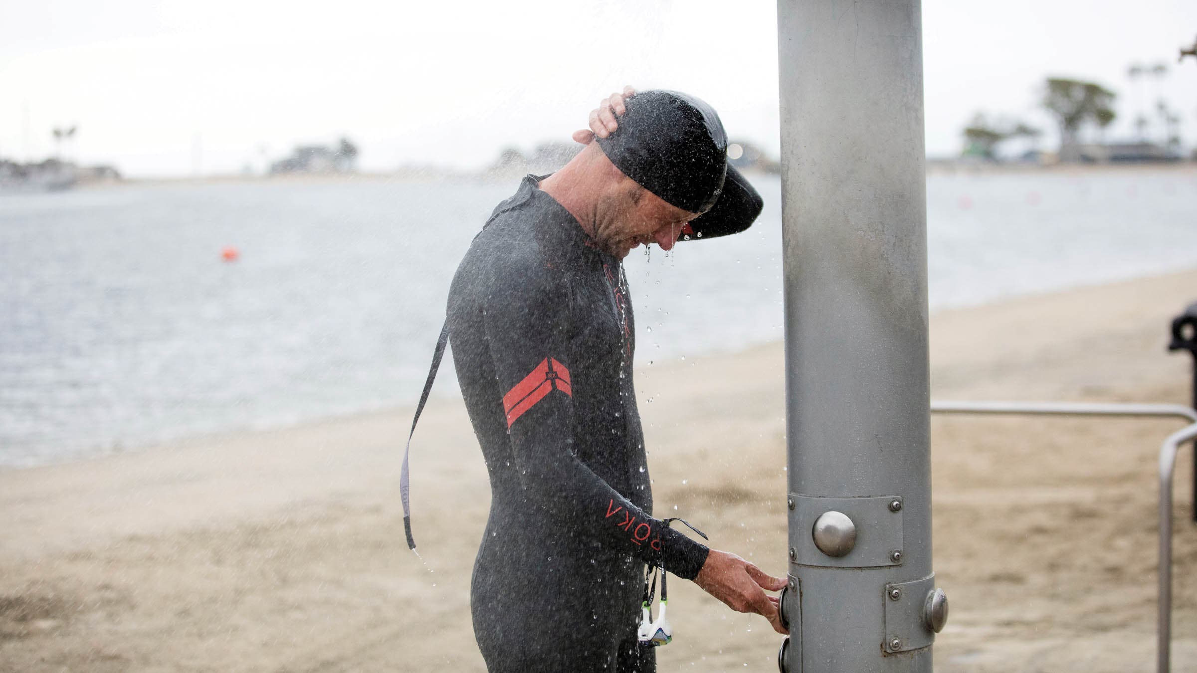 Man in a wetsuit taking an outdoor shower