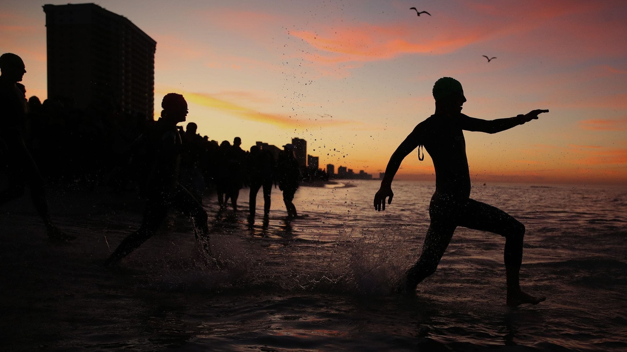 silhouette of athletes run into the ocean in wetsuits with sunrise in the background, start of Ironman Florida race