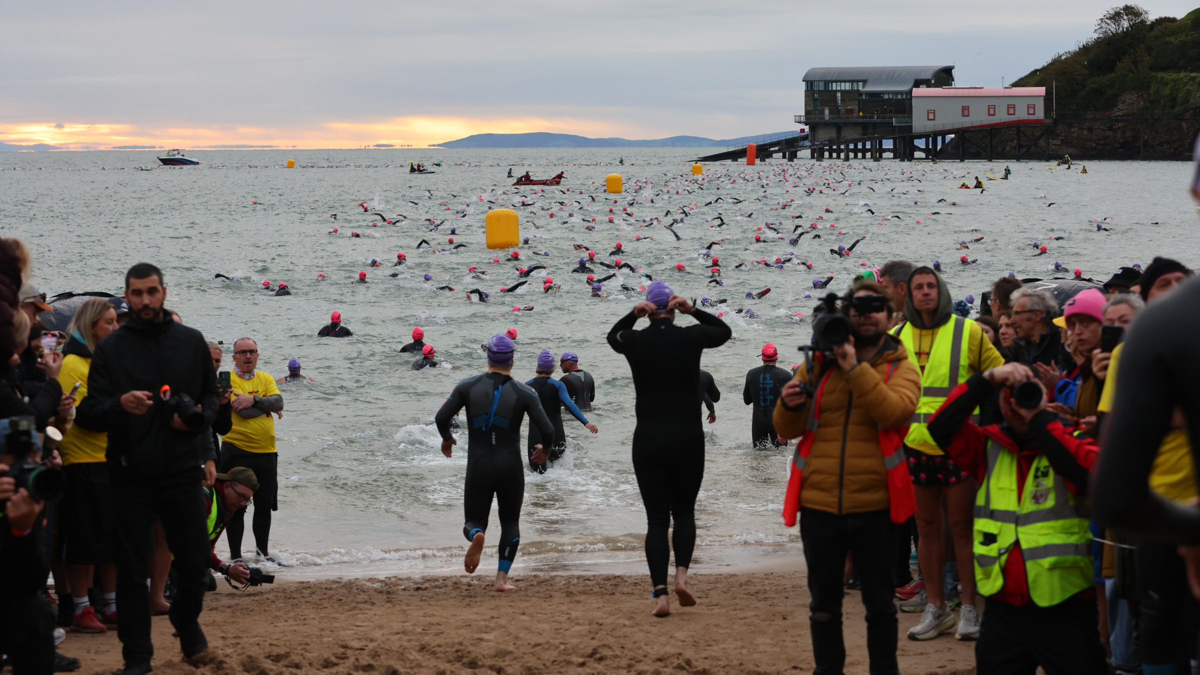 photo of triathletes running into the ocean at North Beach in wetsuits as sun rises over the water