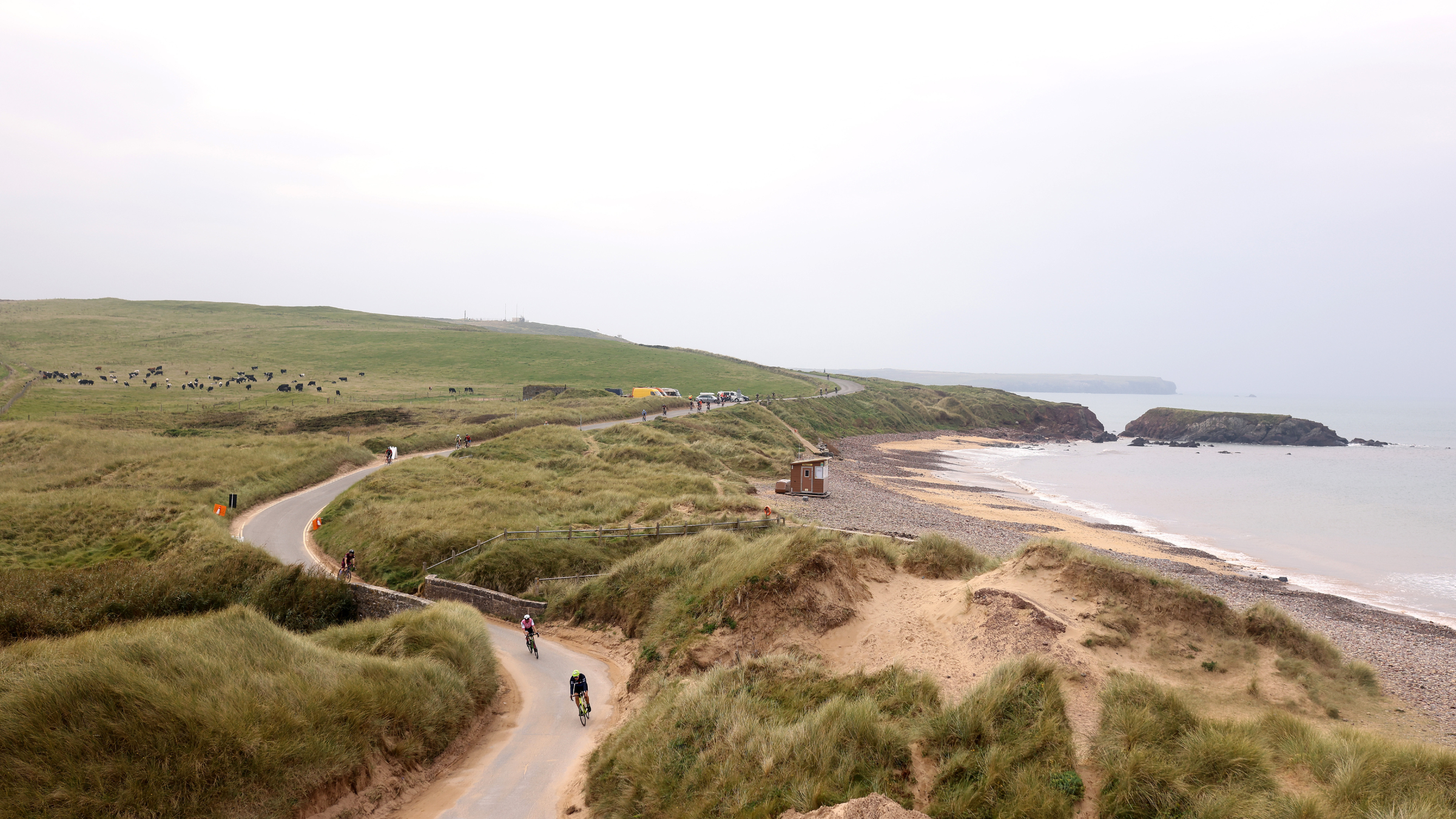 aerial shot of cyclists on winding road alongside coastline