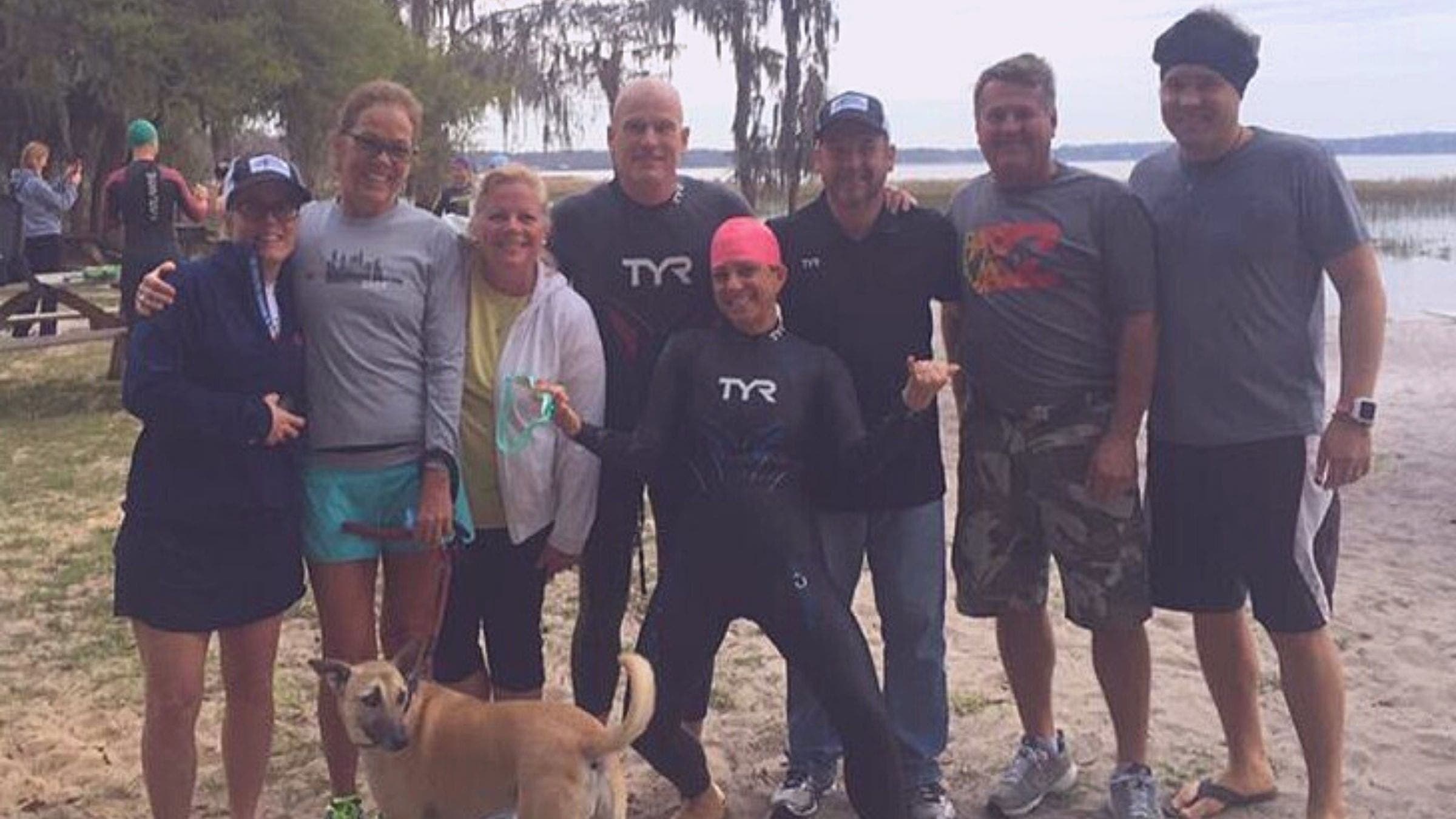 A woman in a wetsuit smiles as she poses in front of her ultra triathlon crew.