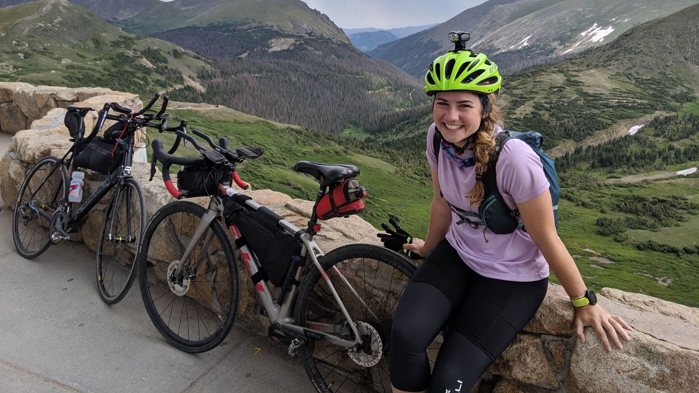 A smiling woman sits on the side of the road next to her bike during an ultra triathlon.