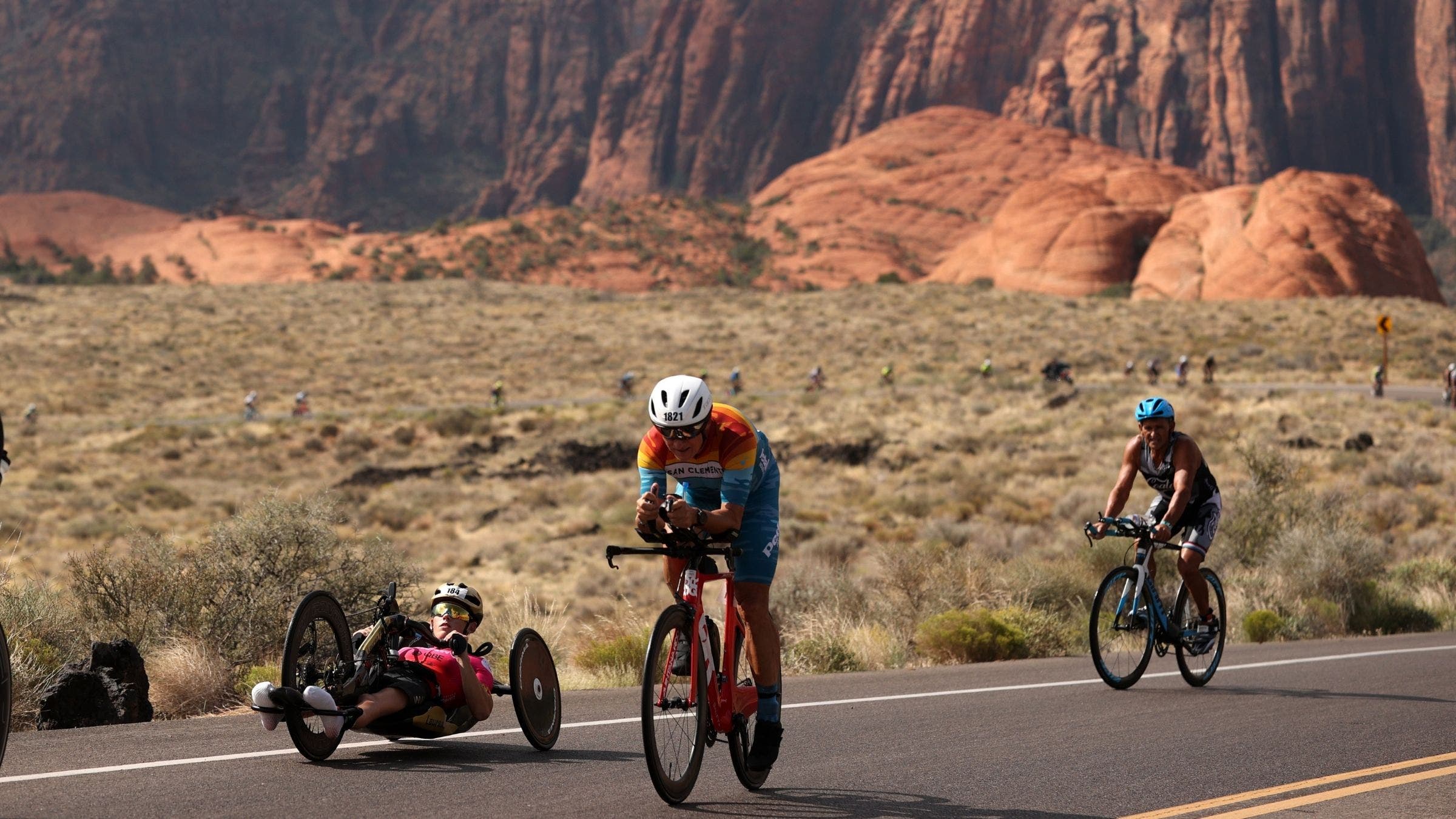 Athletes on the bike at Ironman St. George. One is in aerobars, one is sitting up in the bars, and one is on a recumbent handcycle