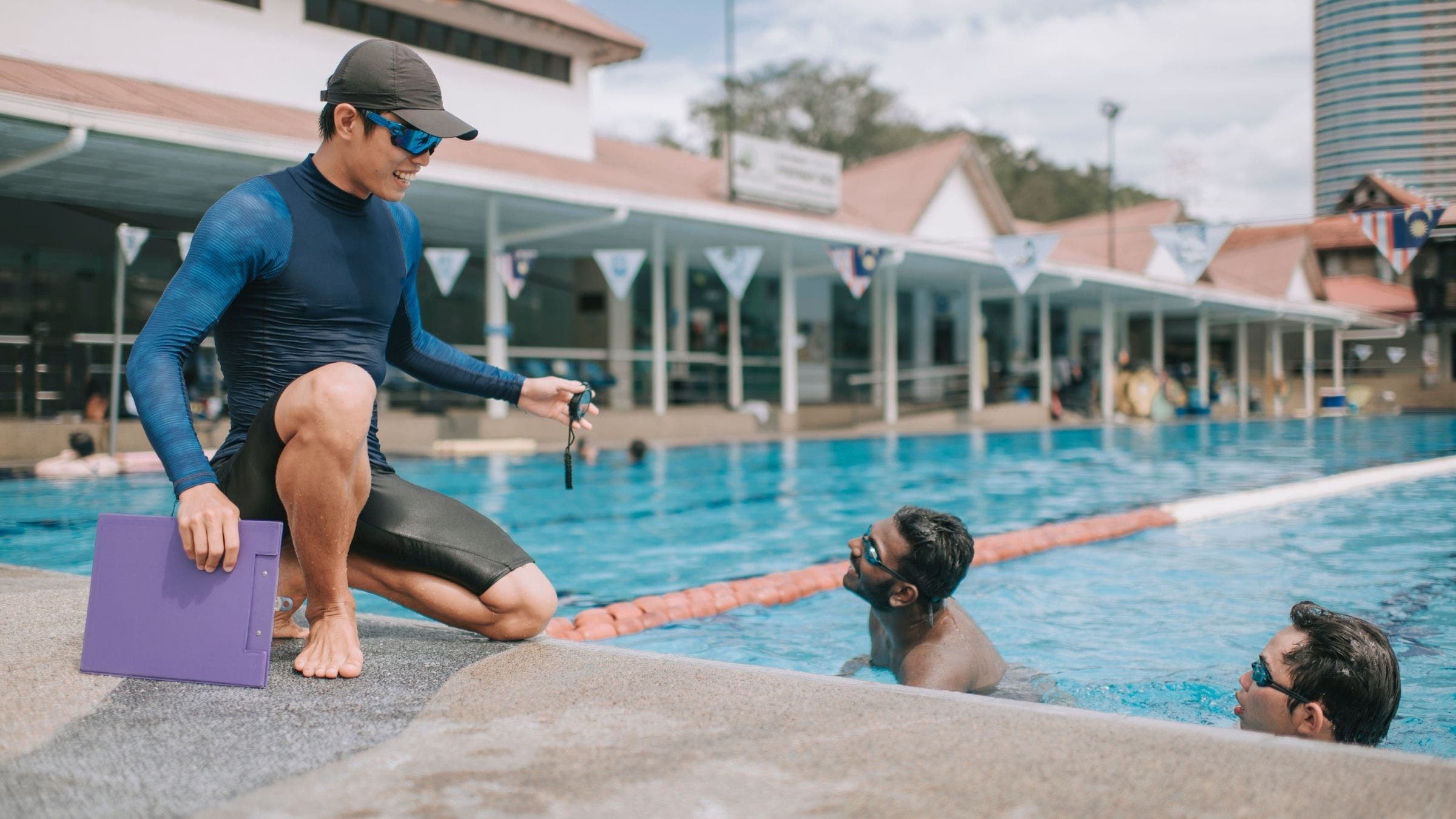 A swim coach explains the purpose of the workout to triathletes in the water.