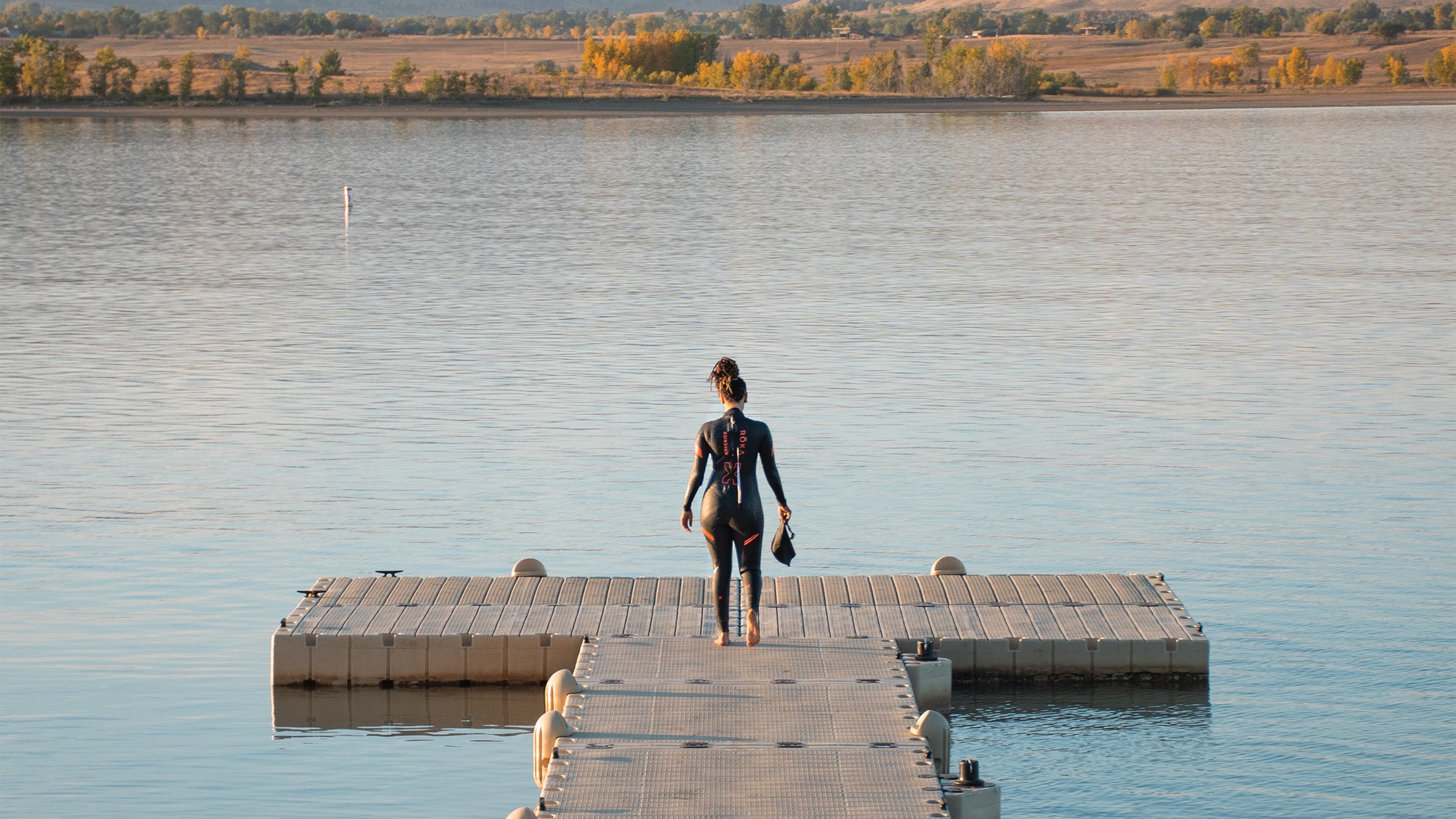 Woman in a wetsuit walking down a small pier to swim