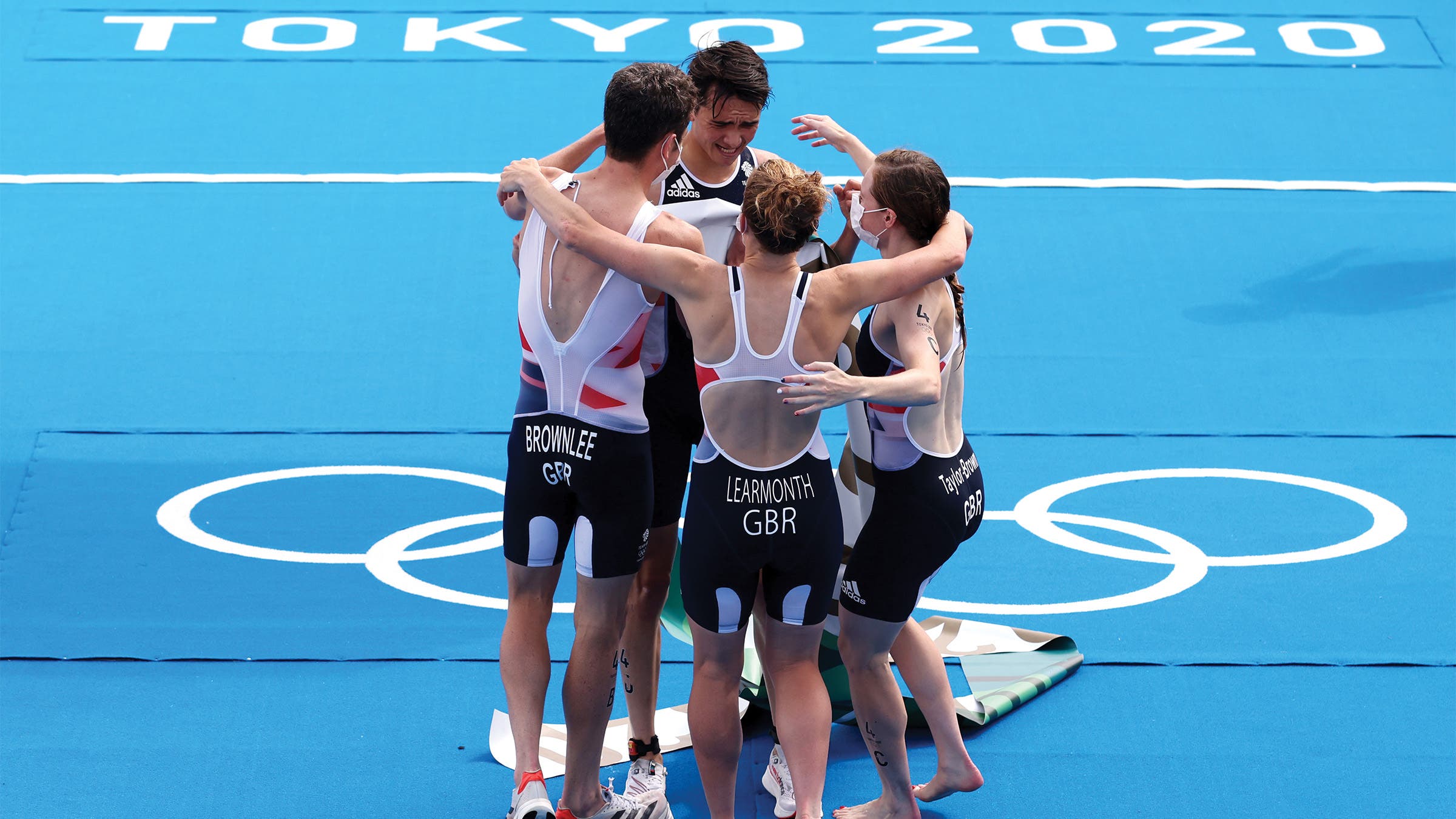 Two men and two women embrace on a blue-lined finish line