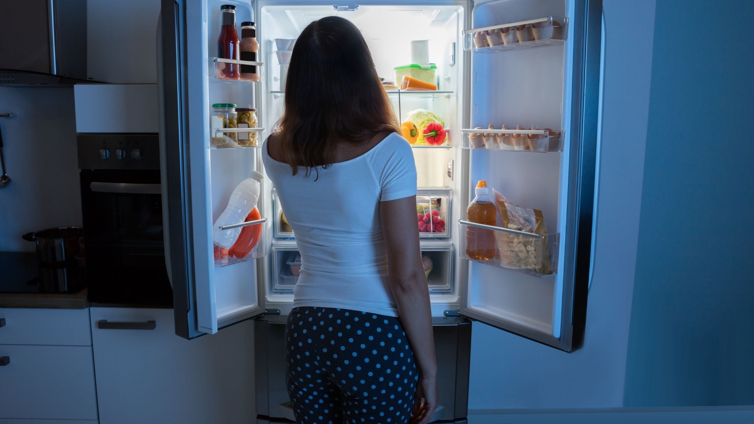 A woman looks in the fridge at night, because she is hungry before bed.