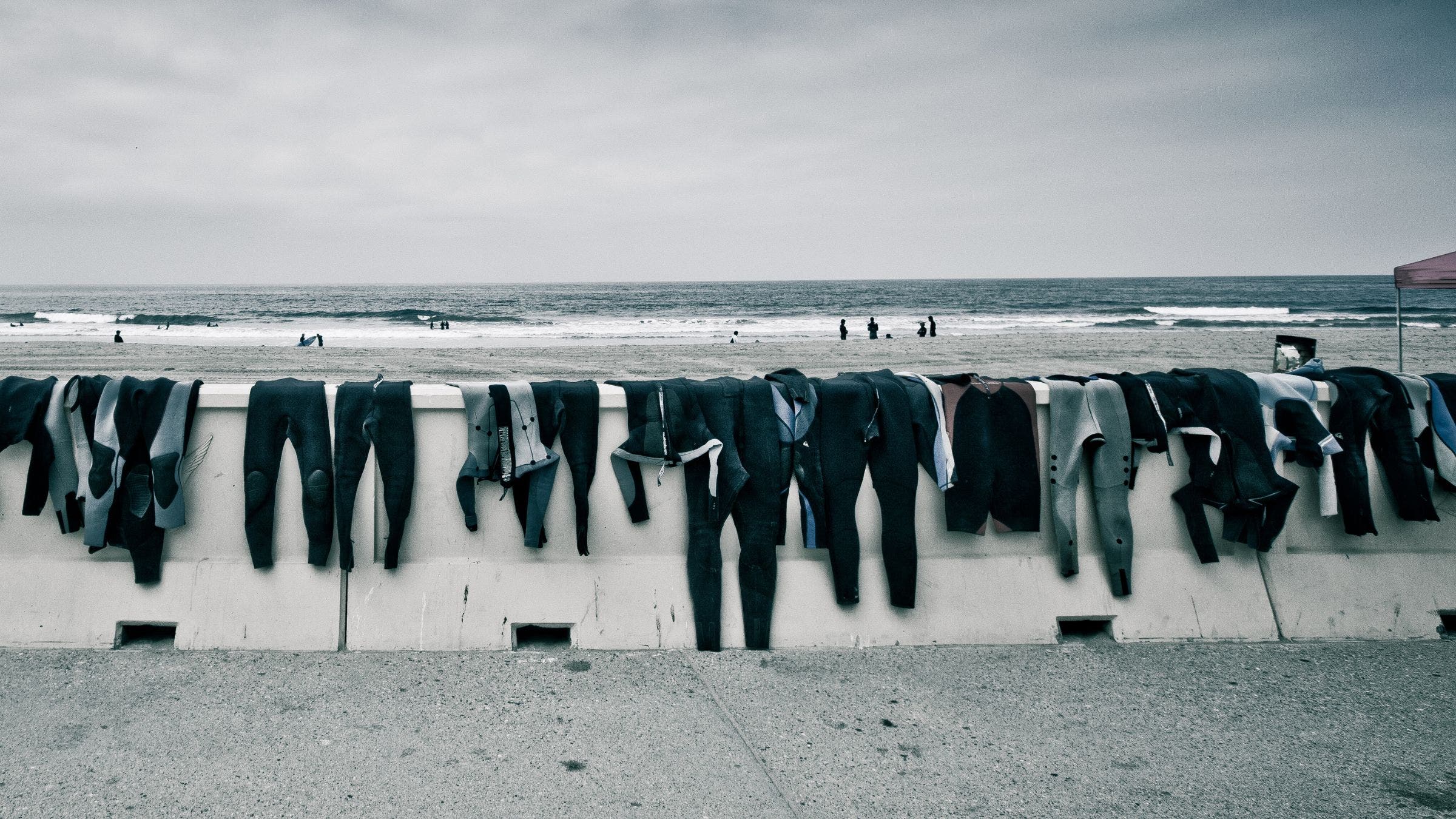 A row of wetsuits drying on a seawall. How to recycle a wetsuit is a common question for many athletes