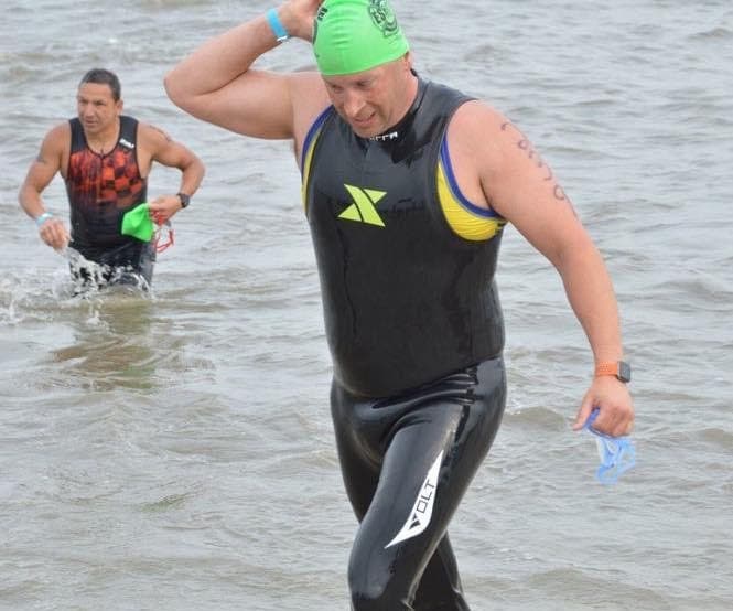 Kyle Smith, wearing a wetsuit for plus-sized triathlete, exits the water of a triathlon