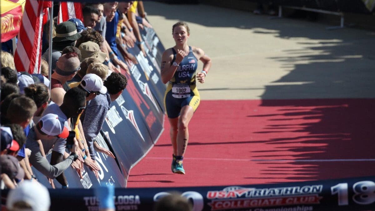 A naval academy women's triathlon athlete runs down the finish chute at a race.