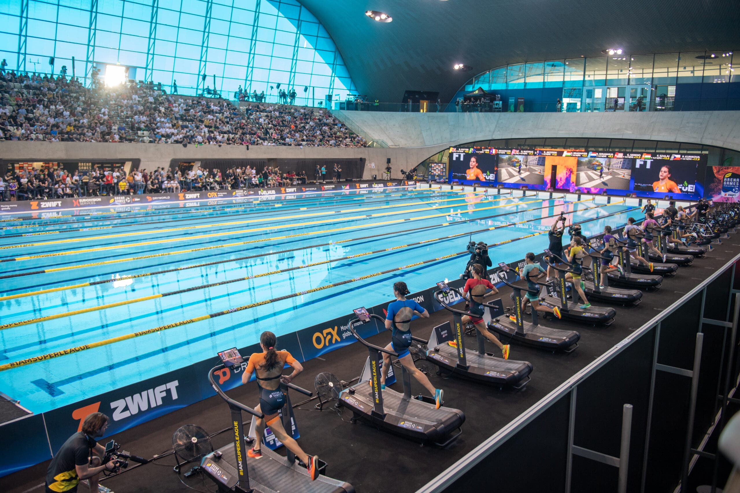 An arena with a pool and athletes running on treadmills on the pool deck.