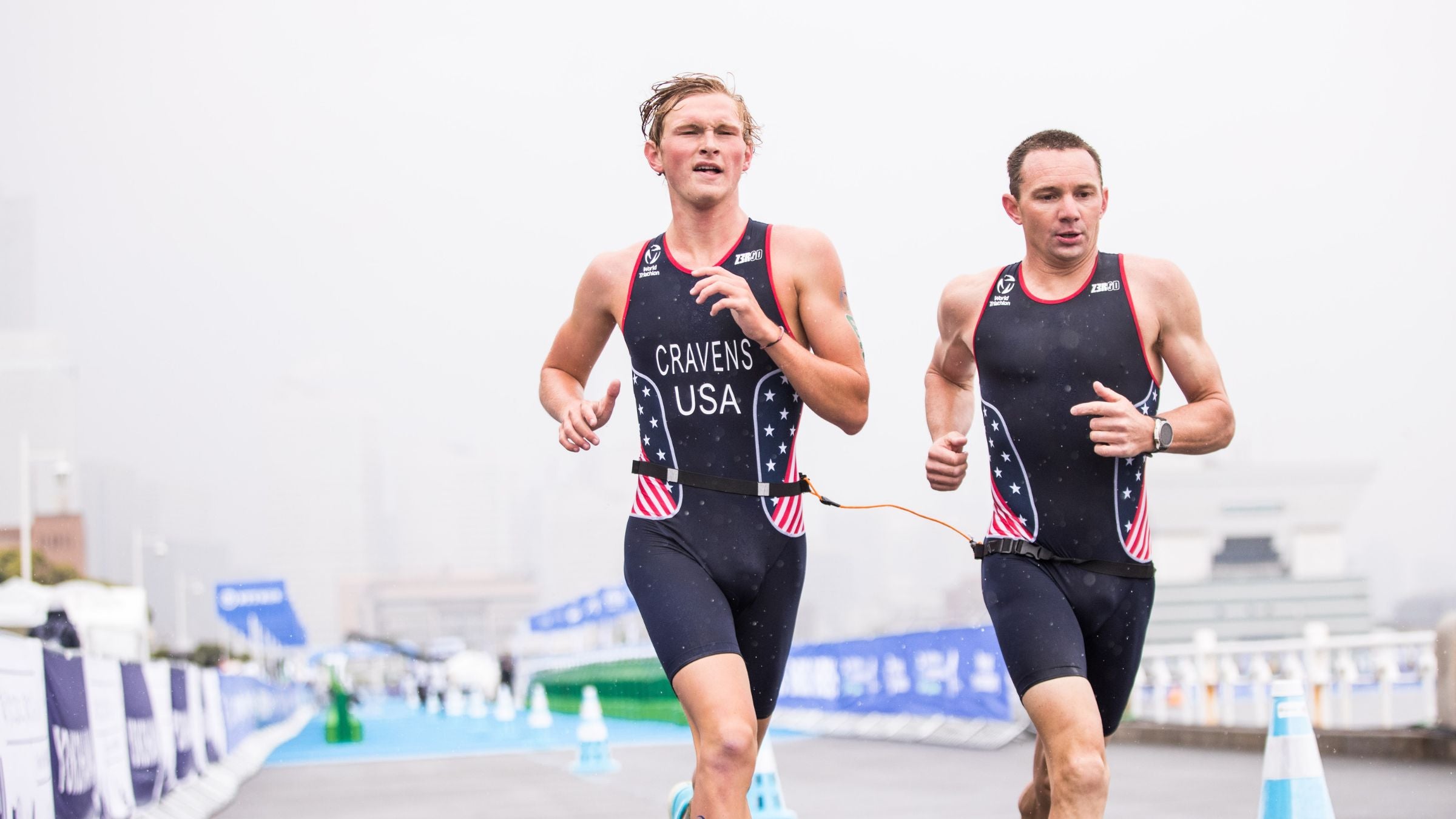 Owen Cravens, a tall blonde visually-impaired triathlete in a red, white and blue triathlon kit, runs alongside his guide, Ben Hoffman, dressed in similar attire.