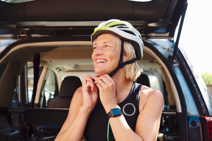 A woman puts on a bike helmet the right way, with the straps below her chin and earlobes and the helmet covering the forehead.