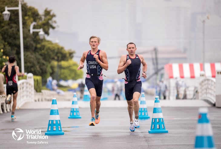 Owen Cravens, a tall blonde visually-impaired triathlete in a red, white and blue triathlon kit, runs alongside his guide, Ben Hoffman, dressed in similar attire.