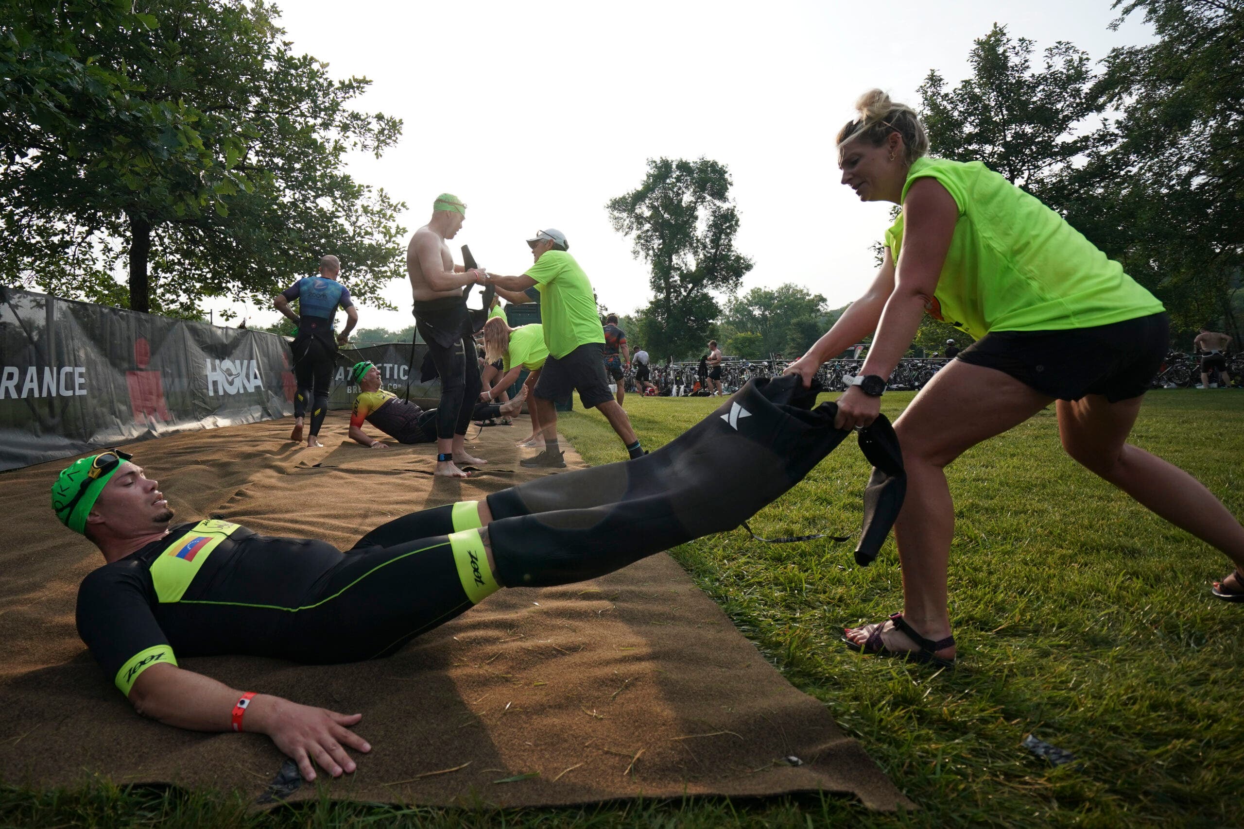 A volunteer helps an athlete remove a wet suit after completing the swim leg of the 2023 Ironman Des Moines 70.3.