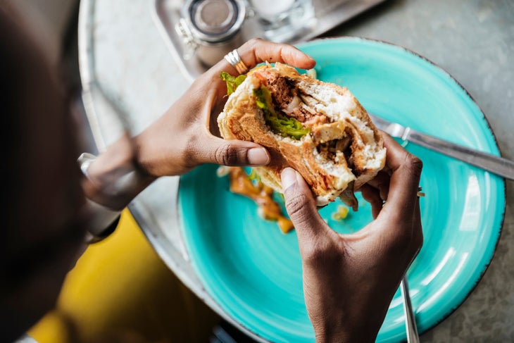 A close up of a woman eating a vegan meatless hamburger in a local cafe with friends.