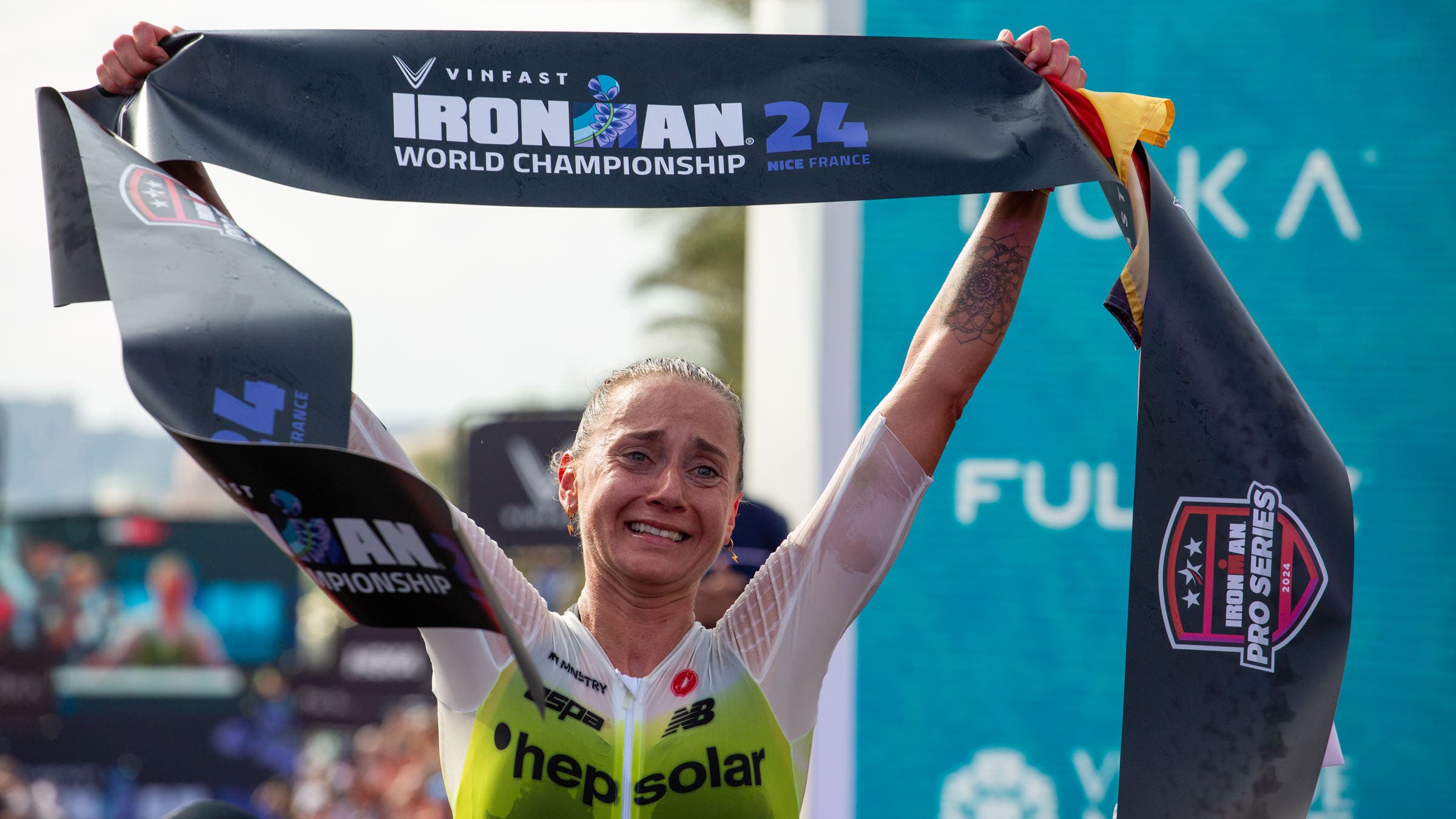 Laura Philipp holds the finish line banner high after winning the 2024 Ironman World Championship title in Nice, France.
