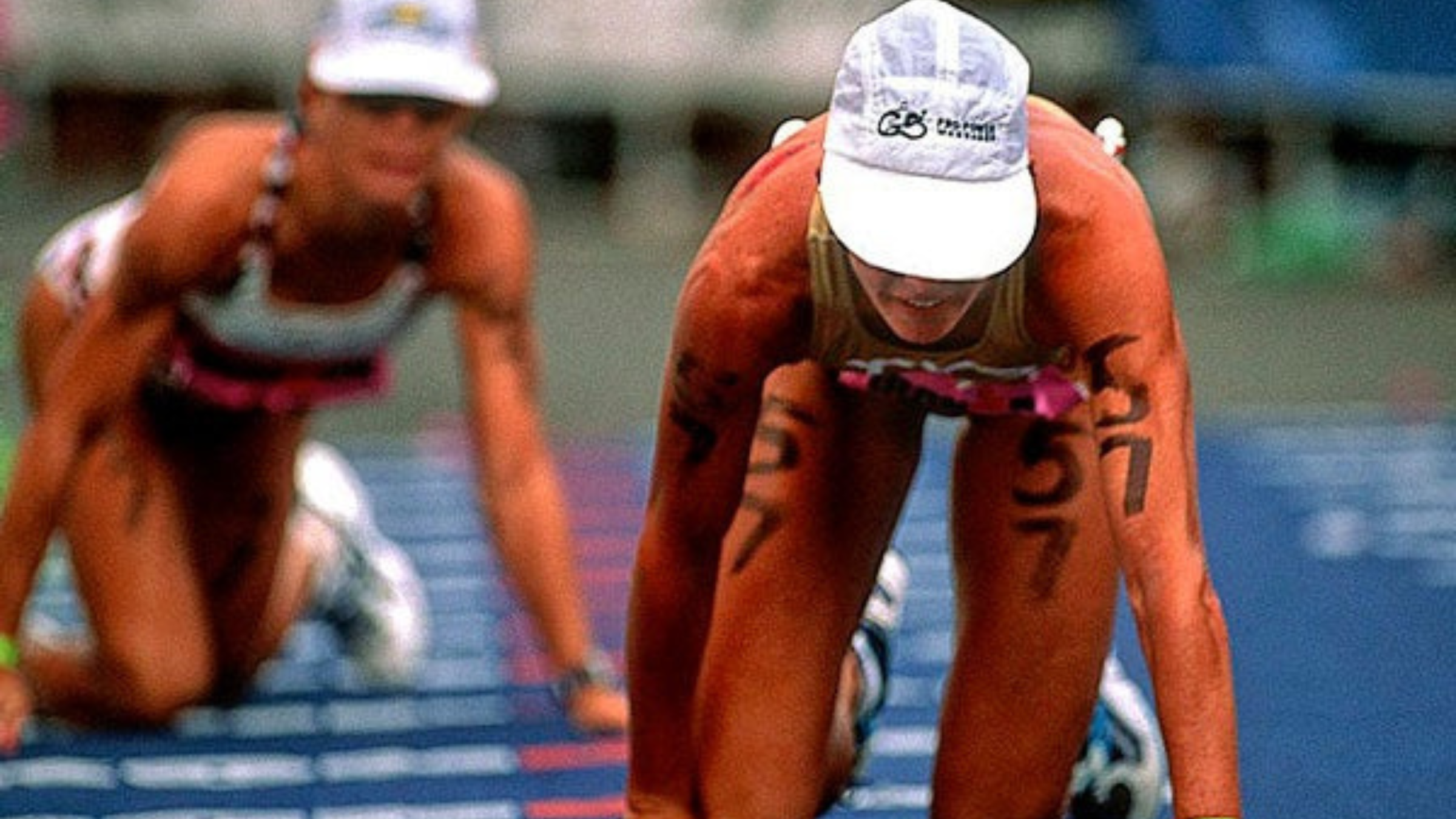 two women in 1990s tri kits and white hats crawl on hands and knees to finish line at Ironman World Championship