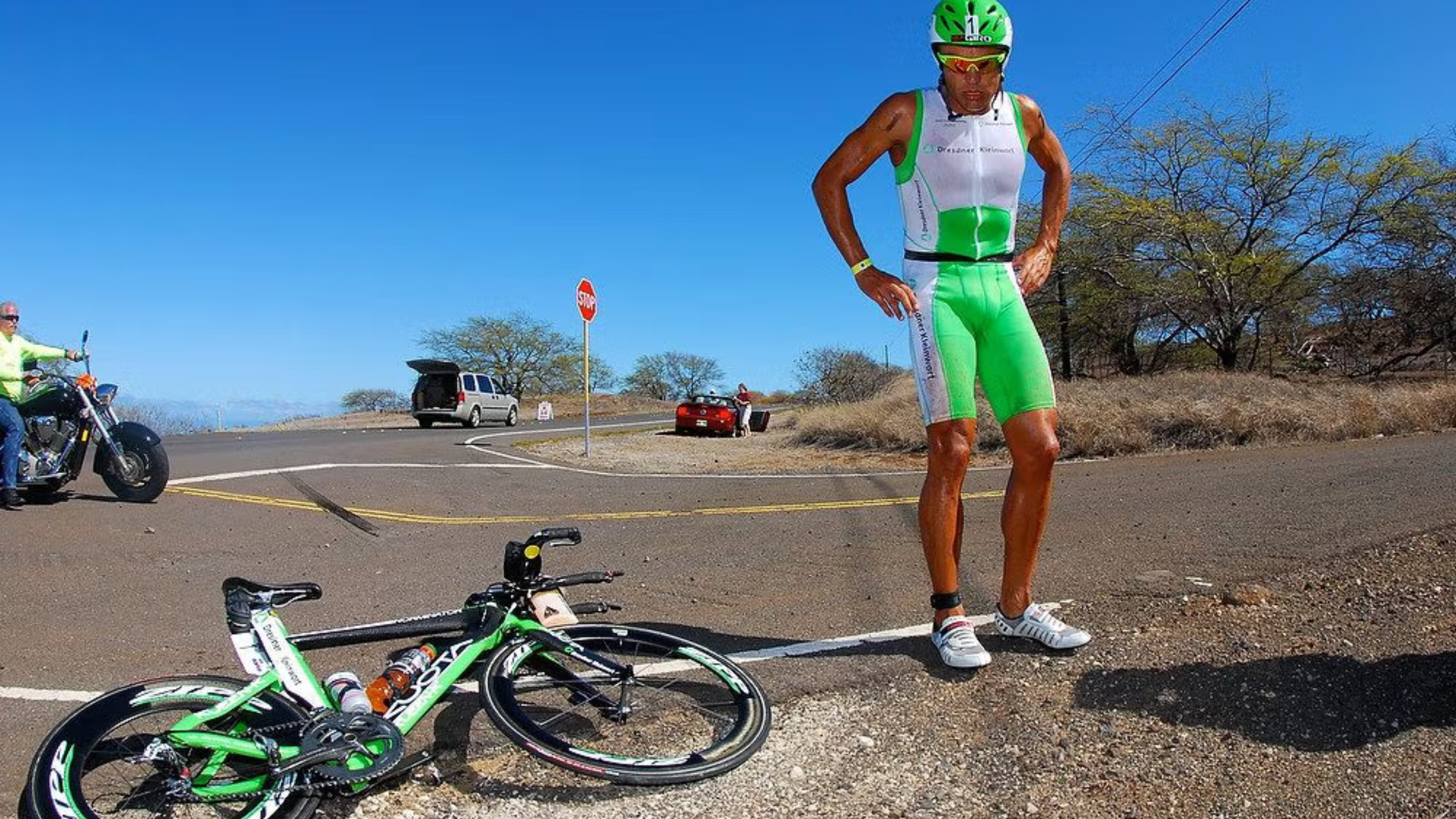 Pro triathlete in his race kit stands with hands on hips next to bike lying on the roadside