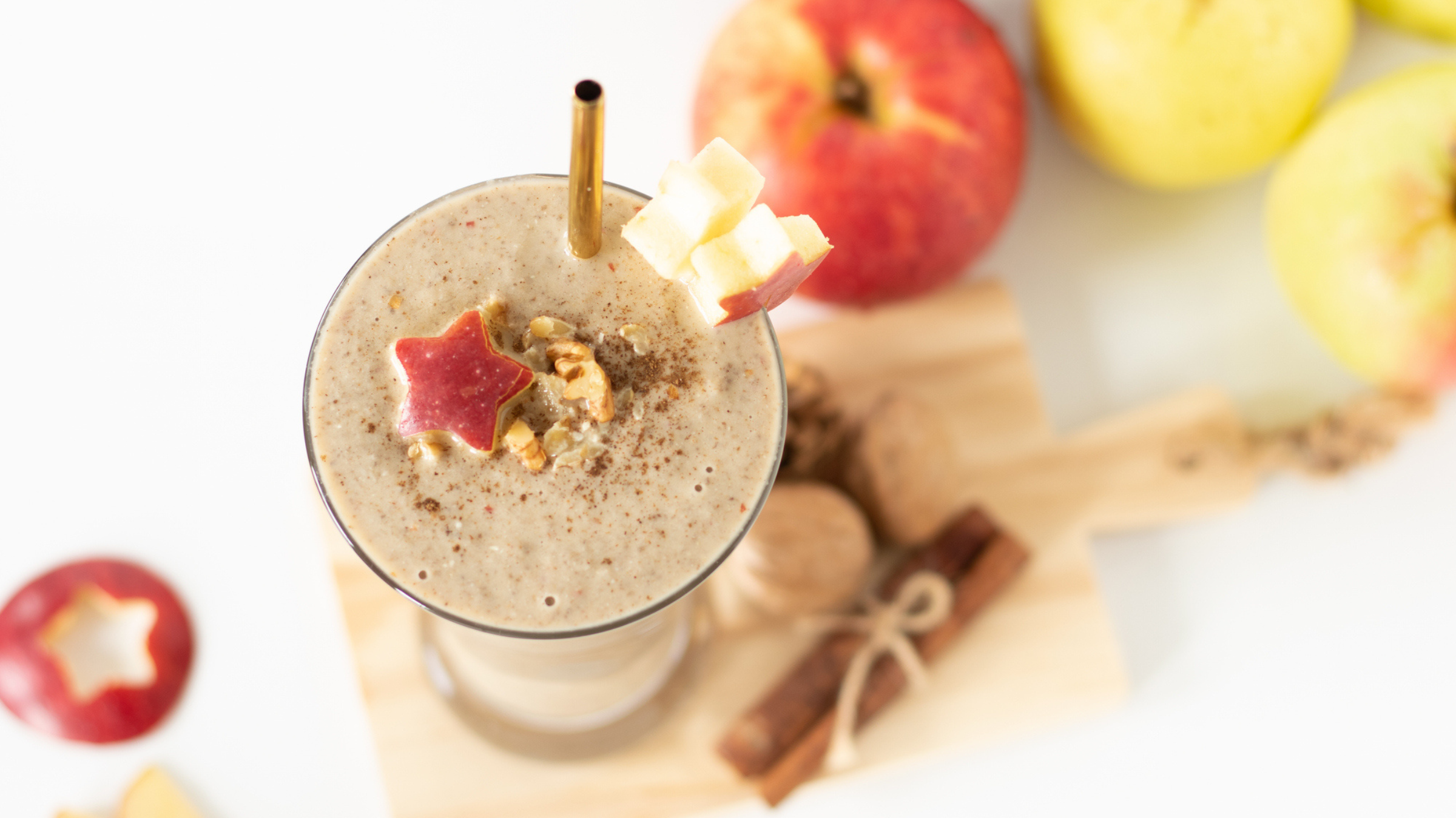 looking down on smoothie in glass with straw and with apples and cinnamon around it on white counter