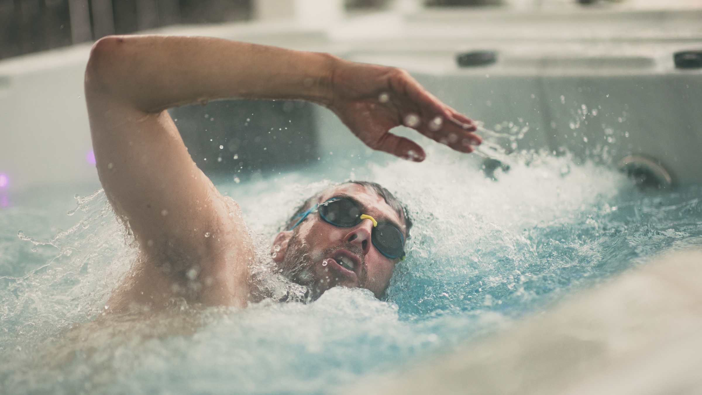 Man swimming in endless-pool style swimming pool with goggles on and looking up to breathe