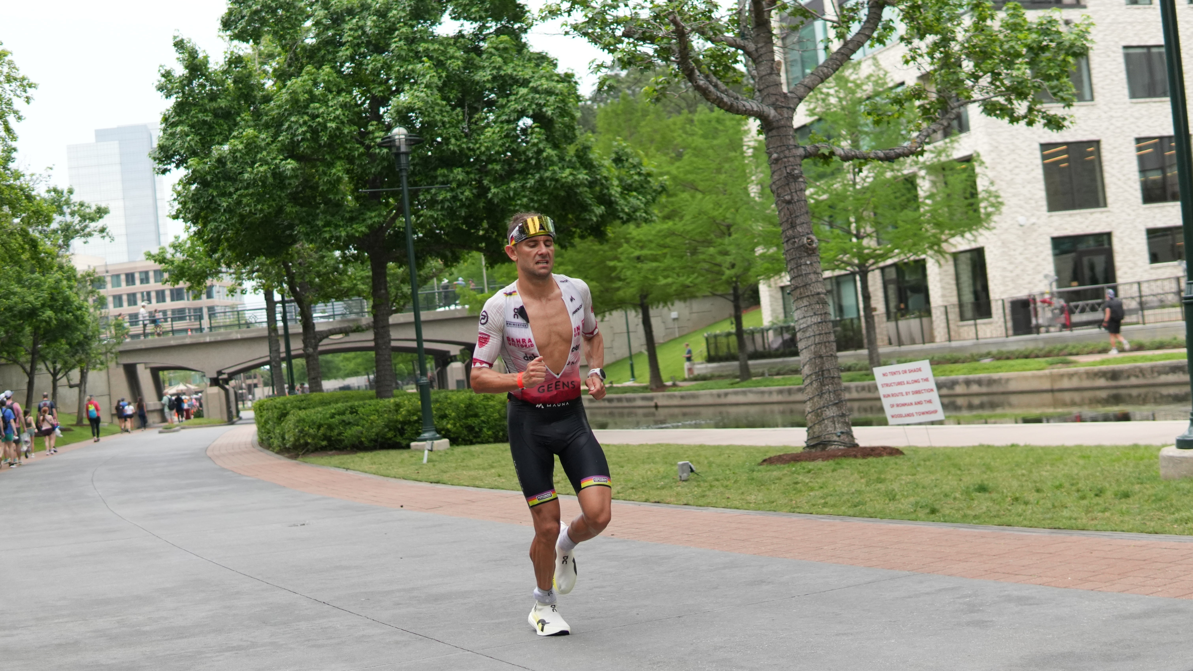 Man wearing a triathlon with unzipped top, running on the road with trees in the background