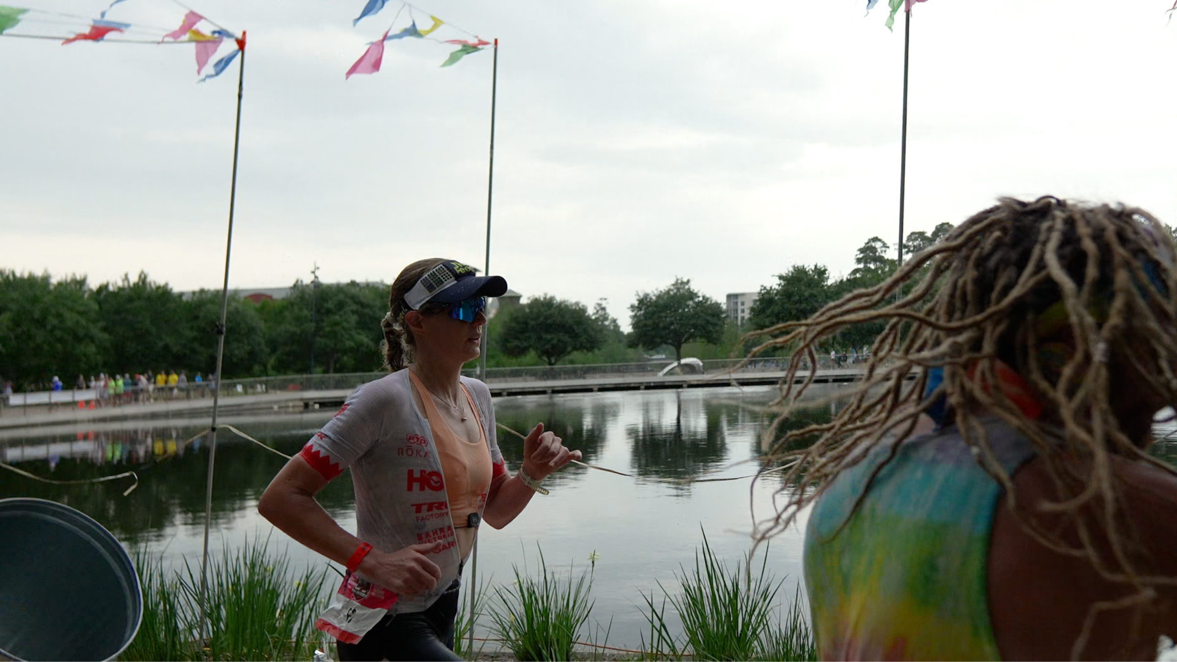 Professional athlete woman wearing a mask and racing set runs along the water with a man wearing dreadlocks cheering her on