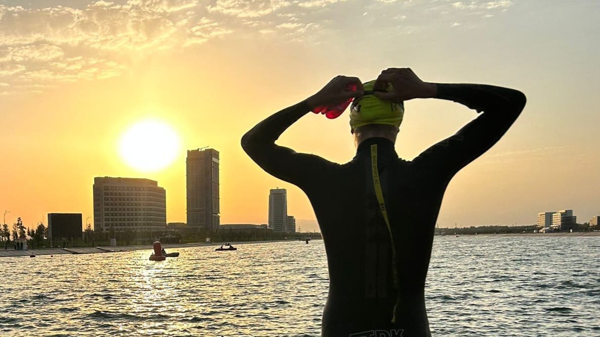 An athlete adjusts his goggles as he prepares for an open water swim at sunrise.