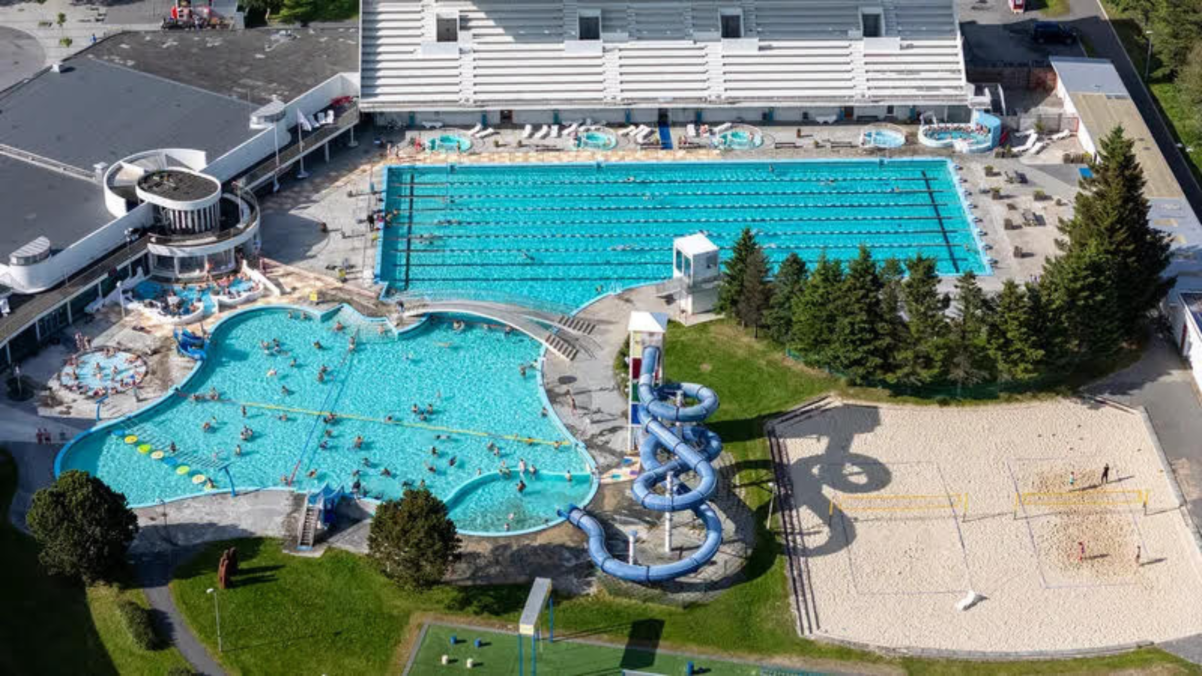 An overhead shot of a huge swimming pool complex with an Olympic-sized pool and a slide