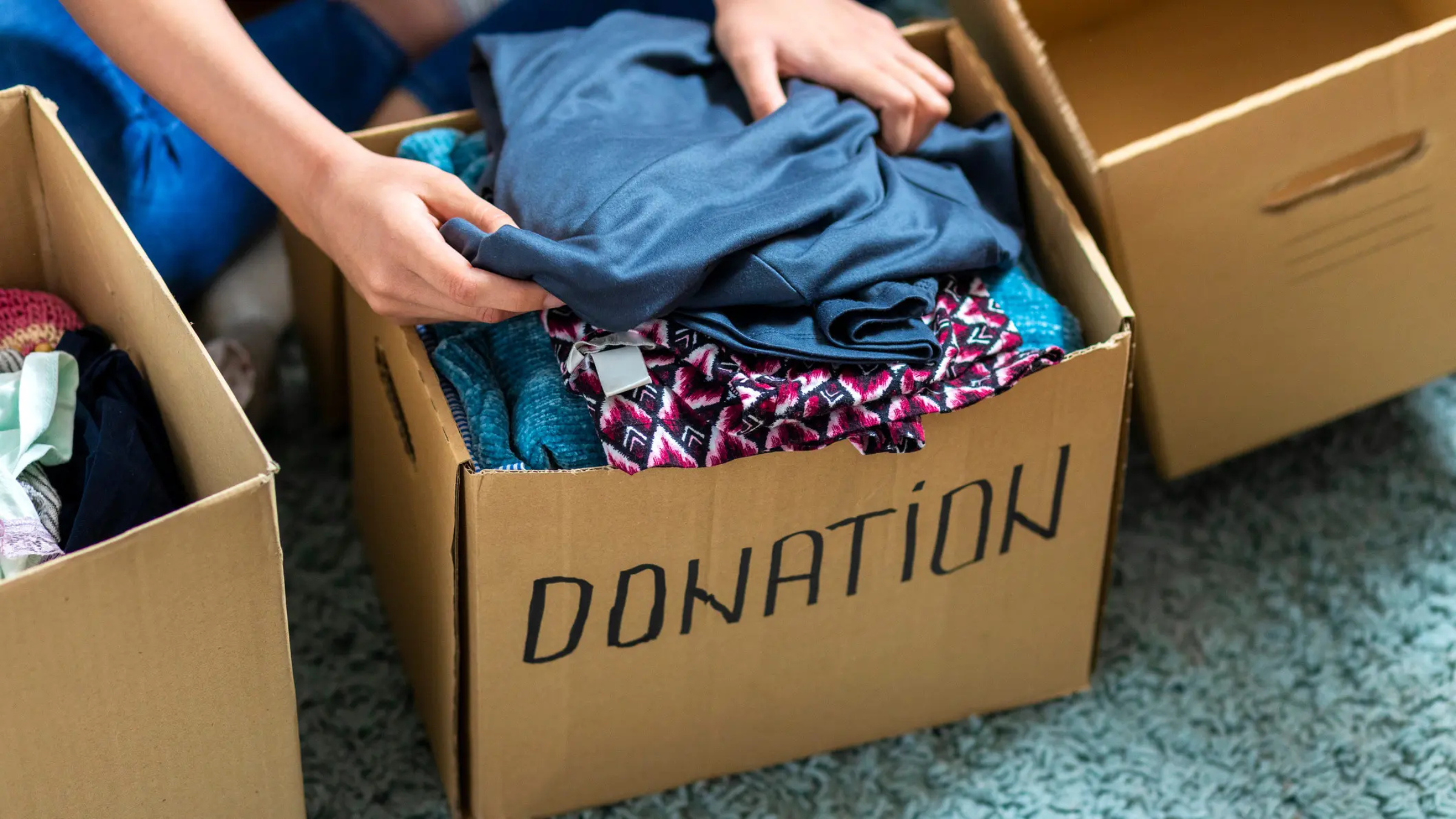 The person's hand loads folded clothing into a labeled cardboard box "gift"