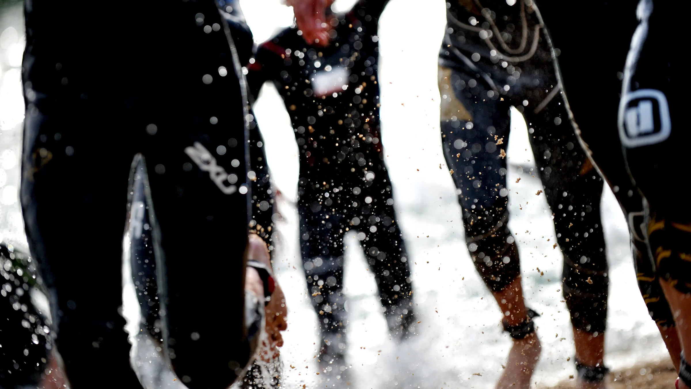 Semi-focused image of people running out of the water wearing triathlon gear, showing their legs and splashes