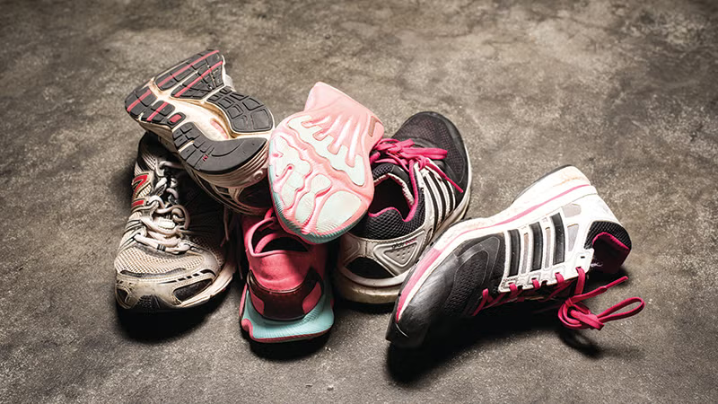 Three pairs of worn running shoes in a pile on the concrete floor