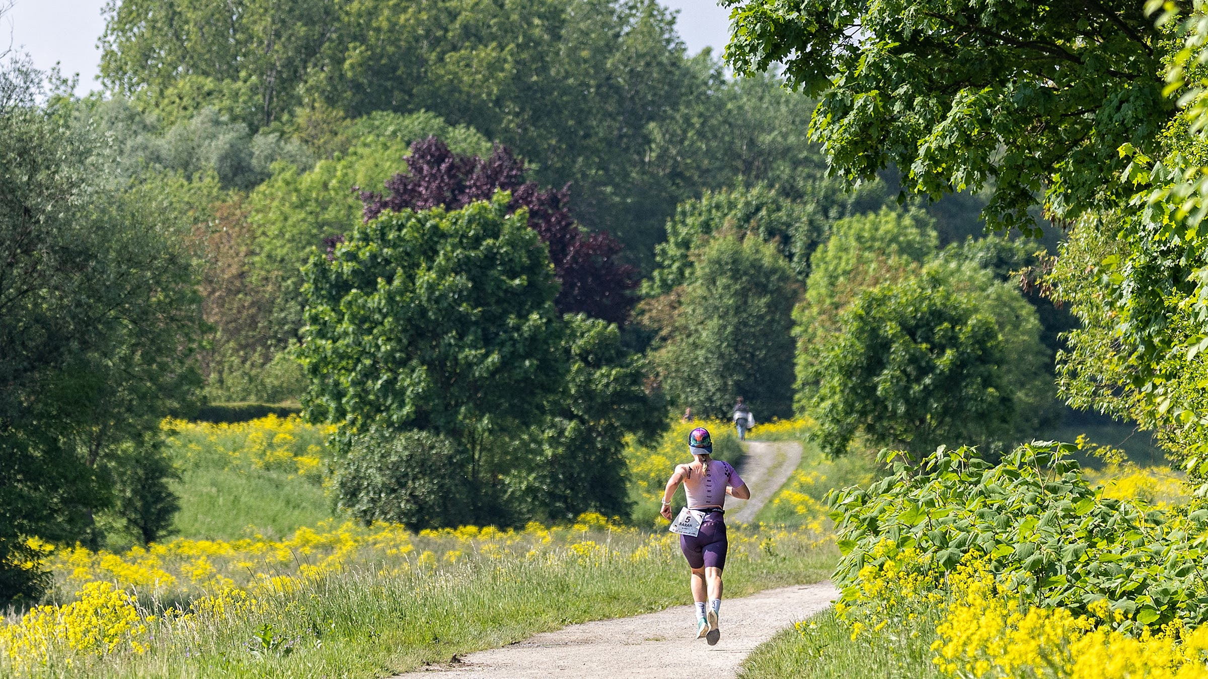 An athlete runs on a path surrounded by lush foliage.