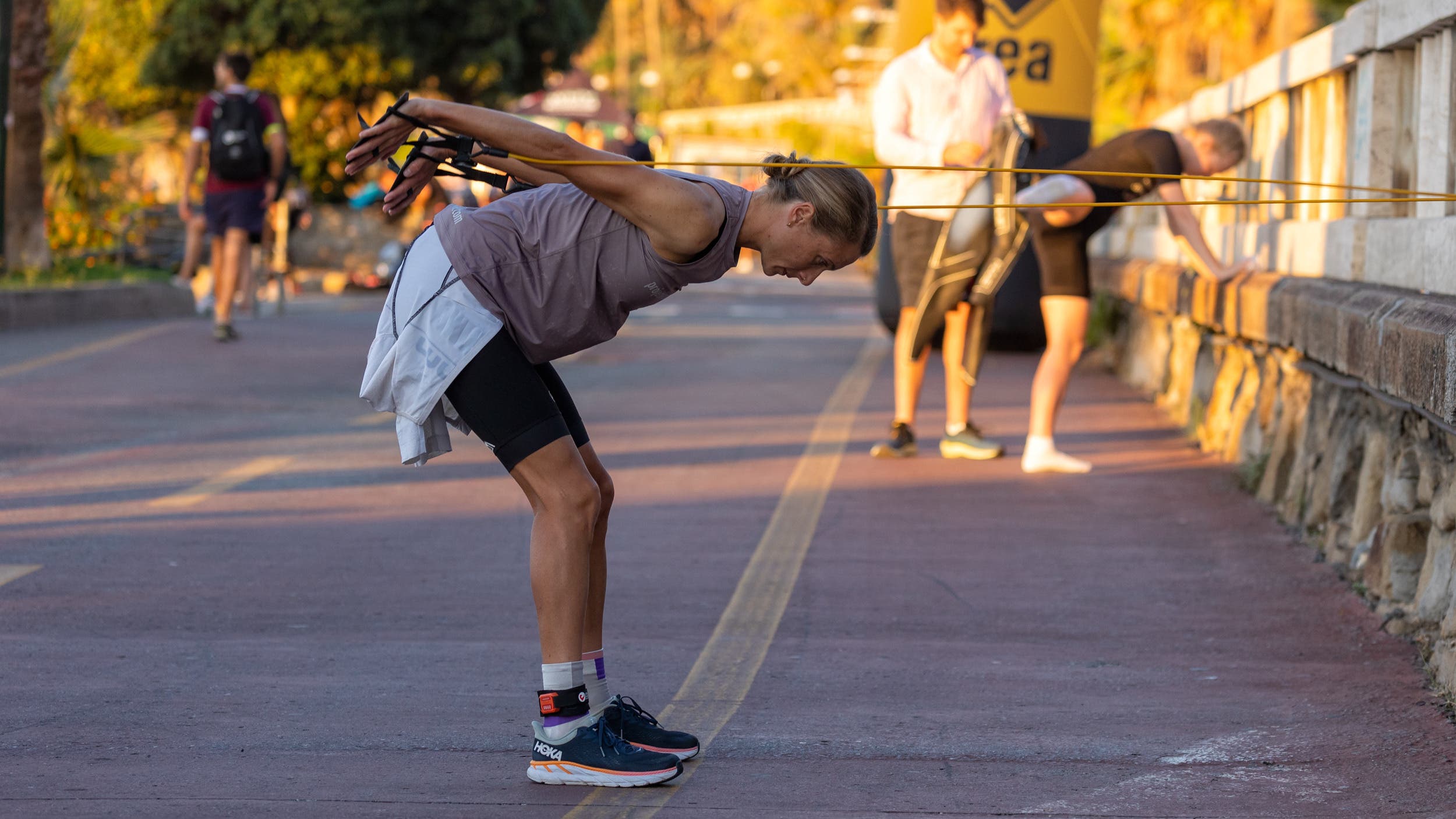 A woman uses stretch cords wrapped around a wall to warm up for a triathlon swim.