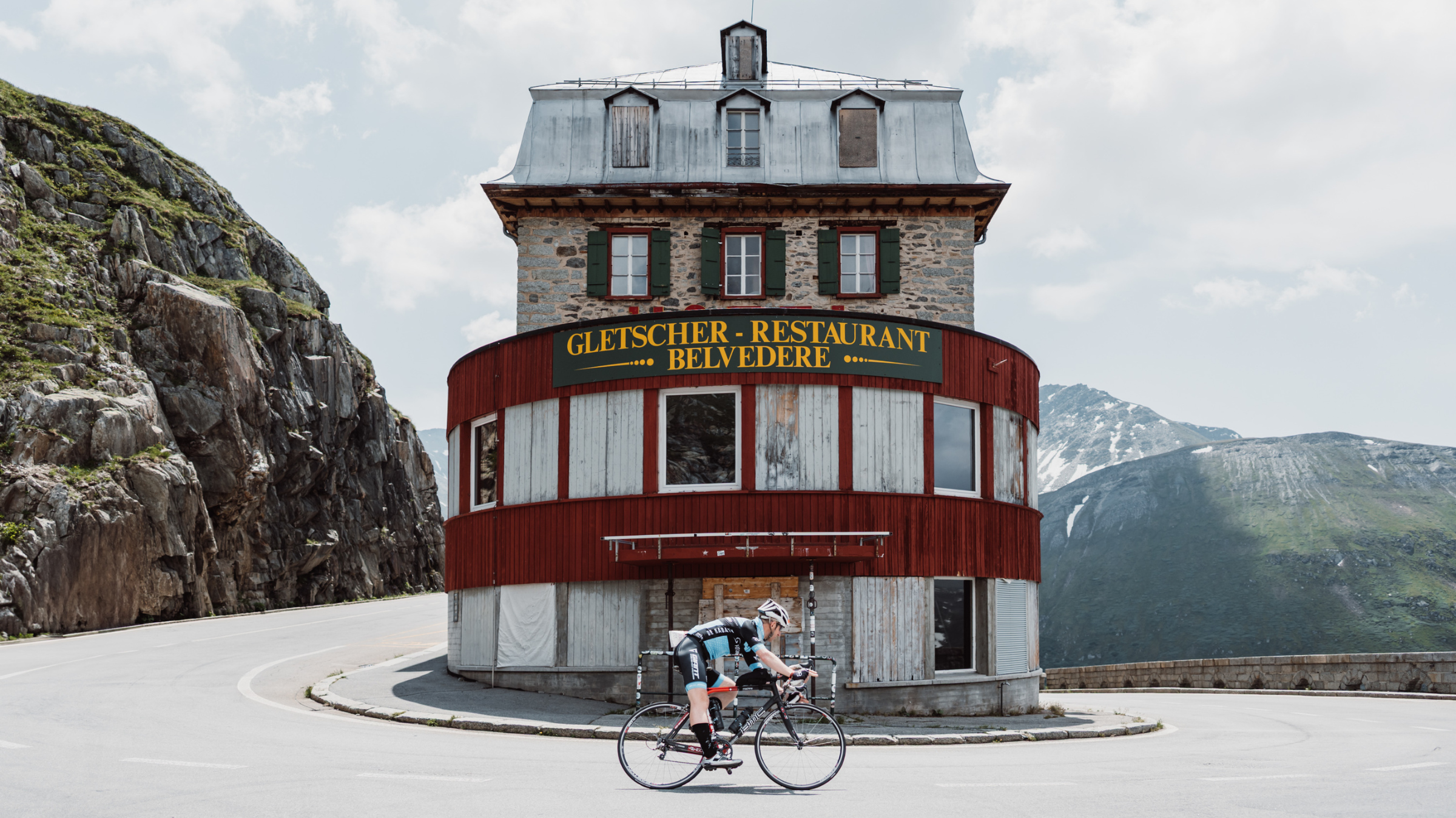 A cyclist rides around a hairpin bend in the Swiss mountains around the circular restaurant building, Swissman Xtreme Triathlon