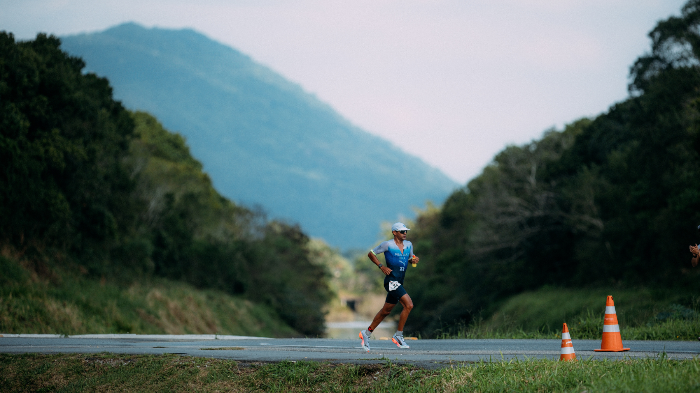 A man runs on the road outside between the hills and trees at Ironman 70.3 Florianópolis