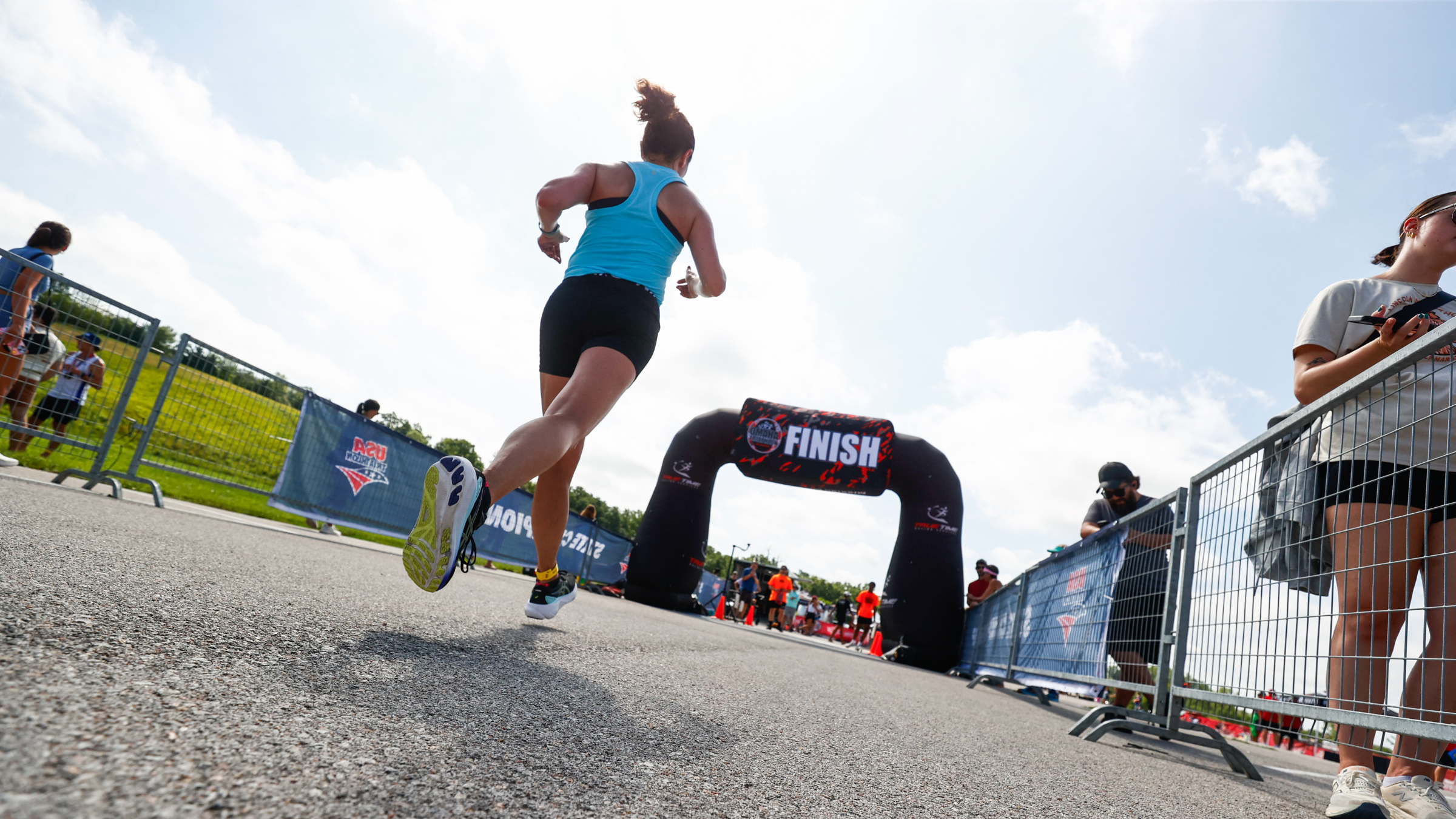A woman wearing a blue shirt and black pants runs on the asphalt towards the finish line arch